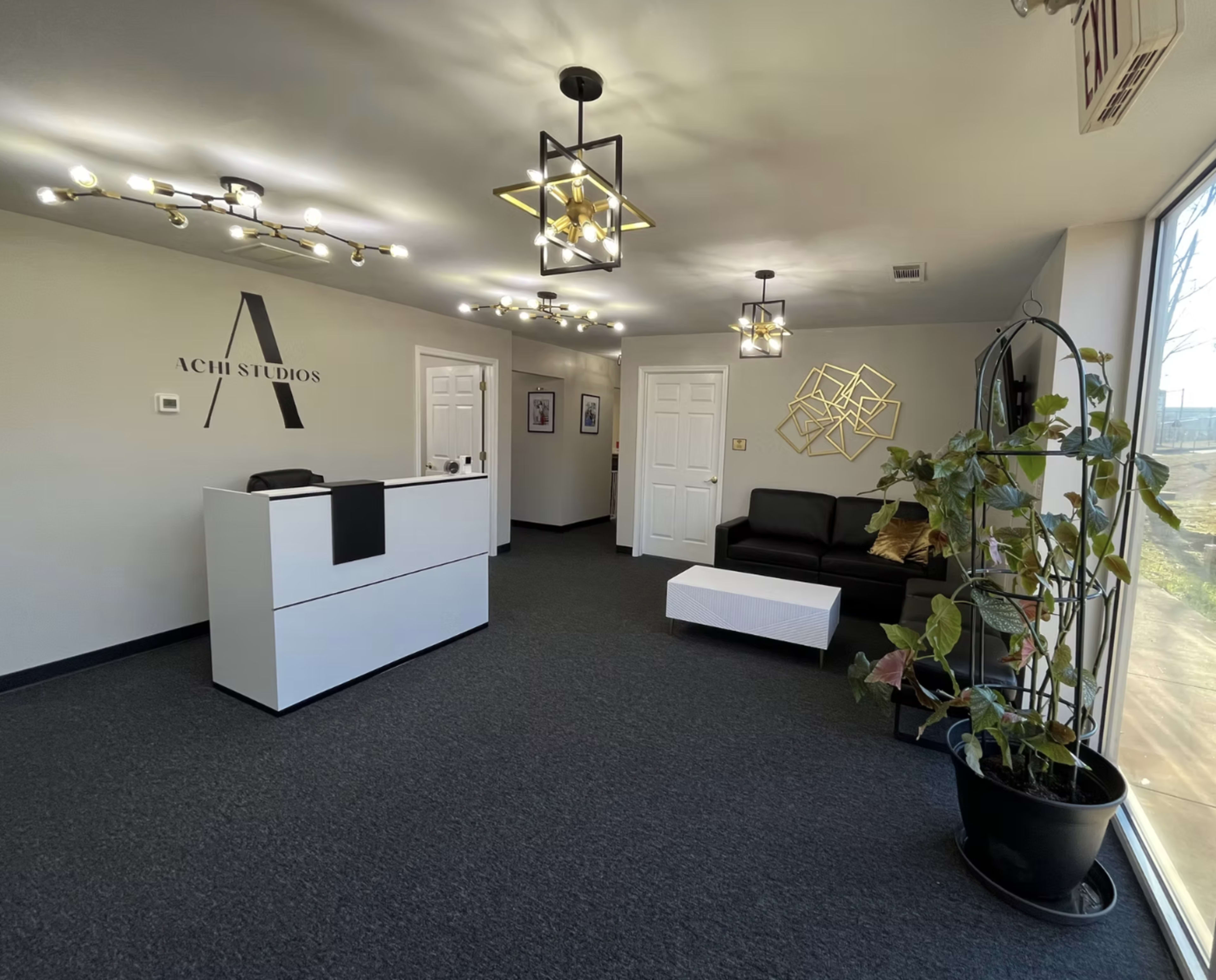 The image shows a modern reception area with a white front desk, a black sofa, a coffee table, and decorative lighting.