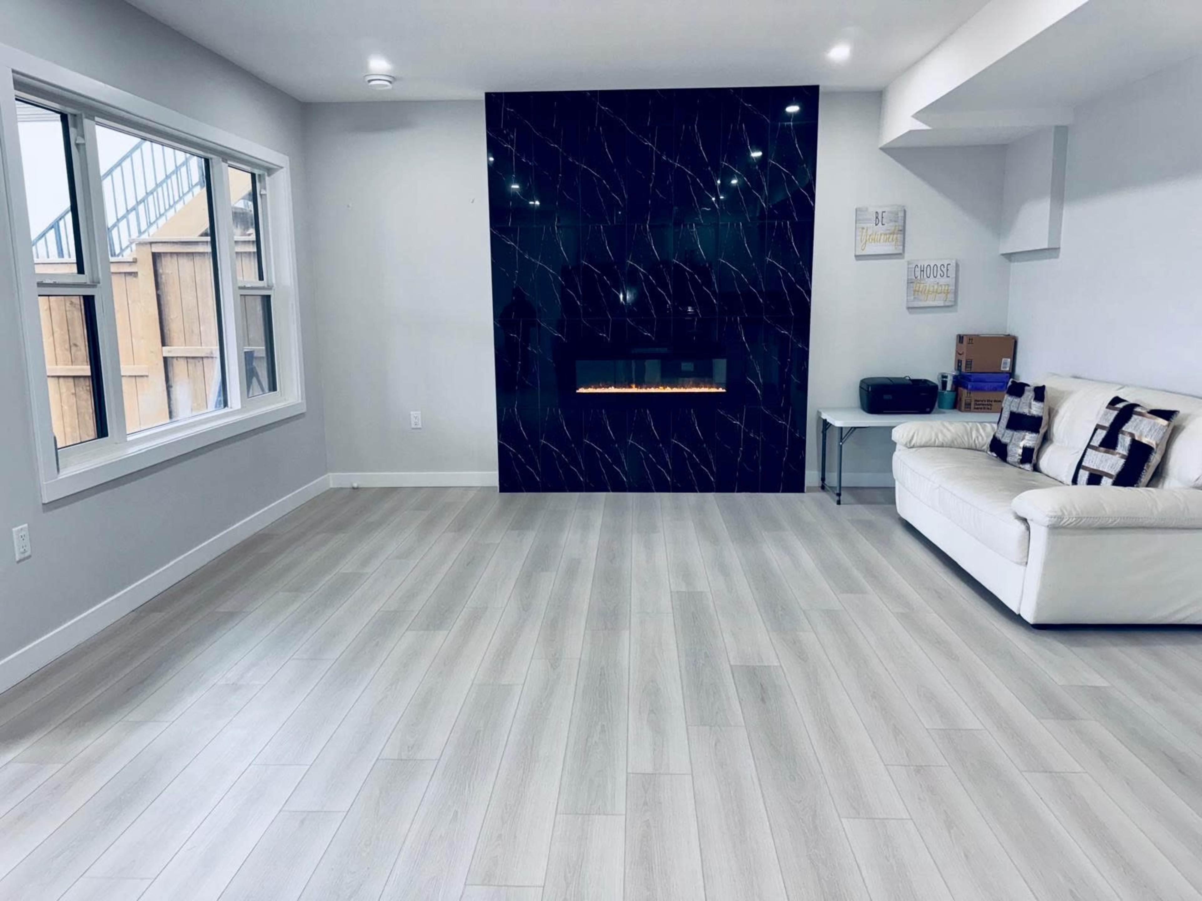 A bright living room features a white sofa, sleek flooring, and a modern black accent wall with a fireplace.