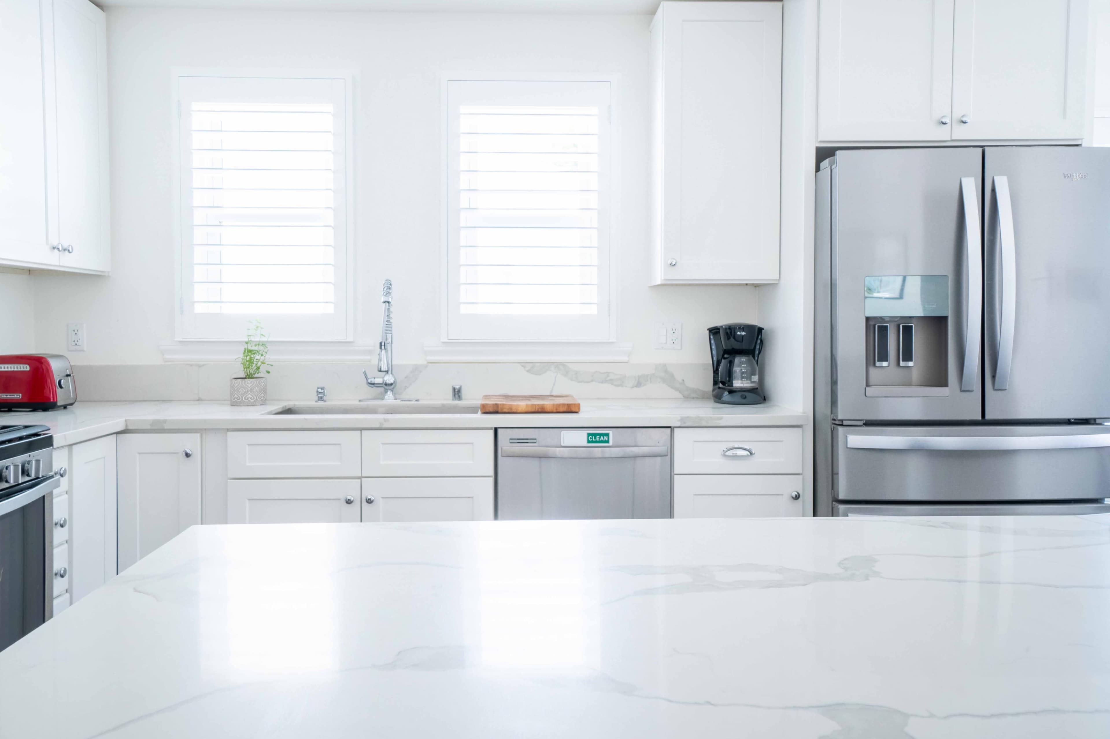 A modern kitchen with white cabinetry, stainless steel appliances, and a large marble island.