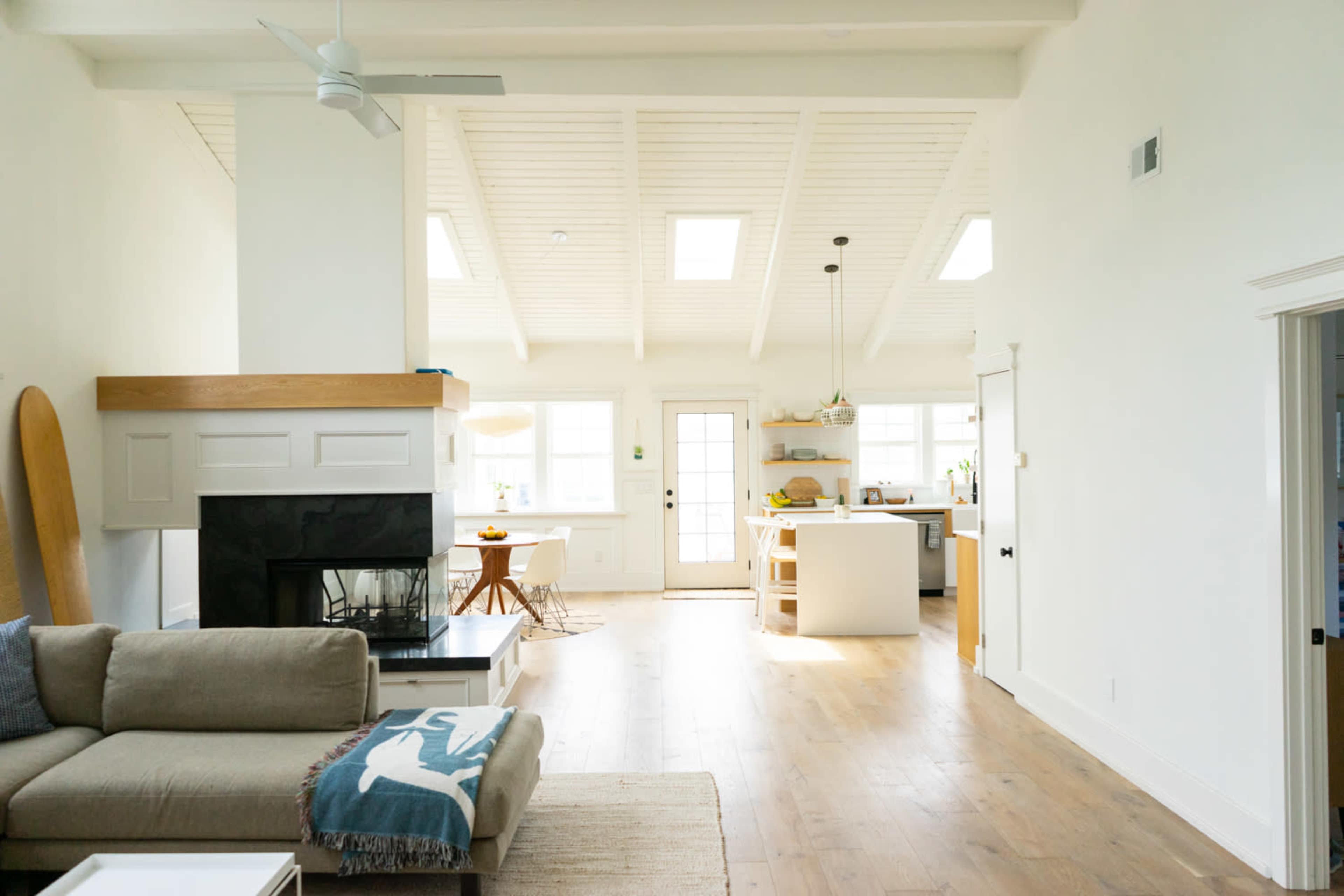 A bright, open living area features a sofa, a fireplace, and a view into a modern kitchen with a dining table.