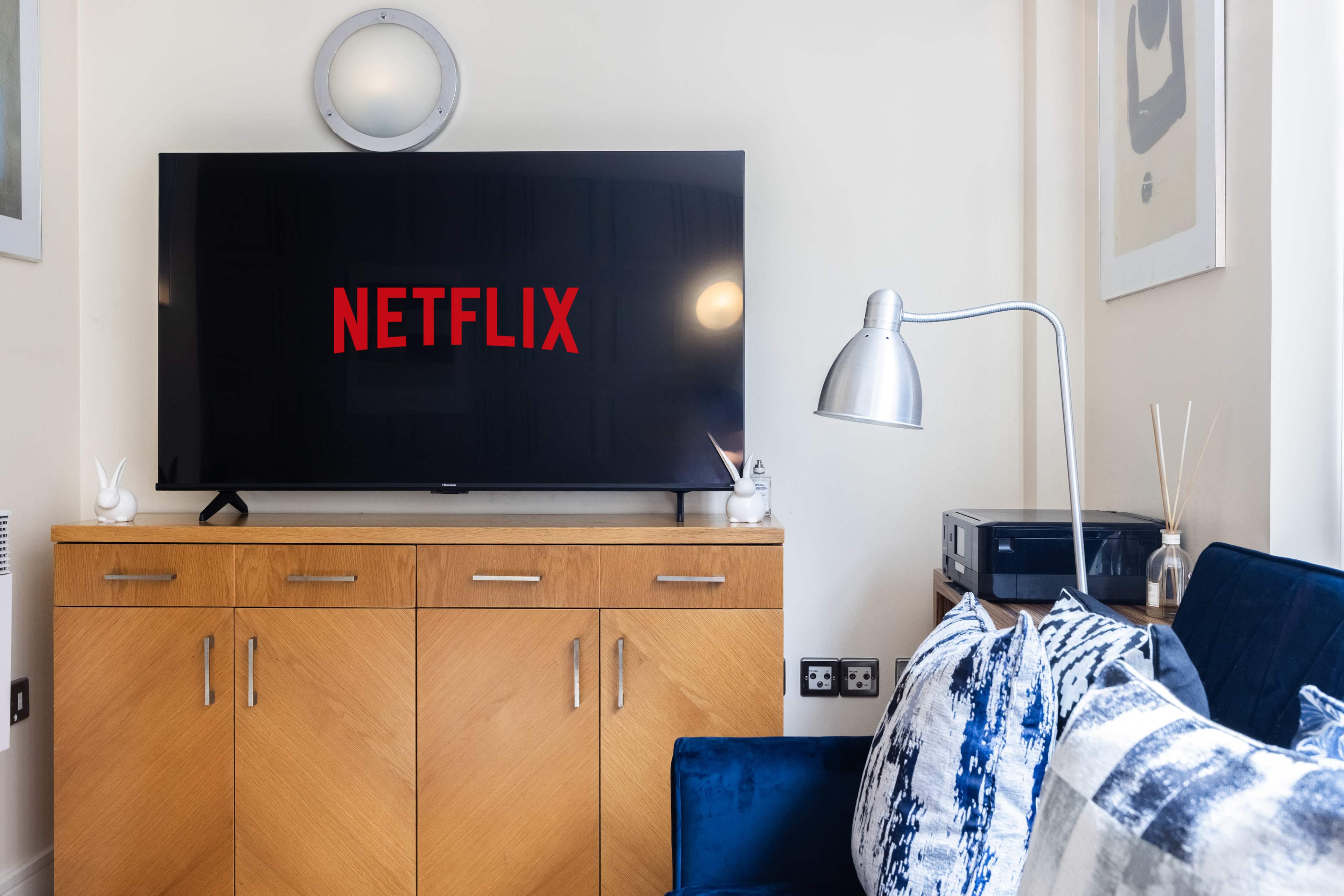 A television displaying the Netflix logo is mounted above a wooden cabinet in a modern living room setting.