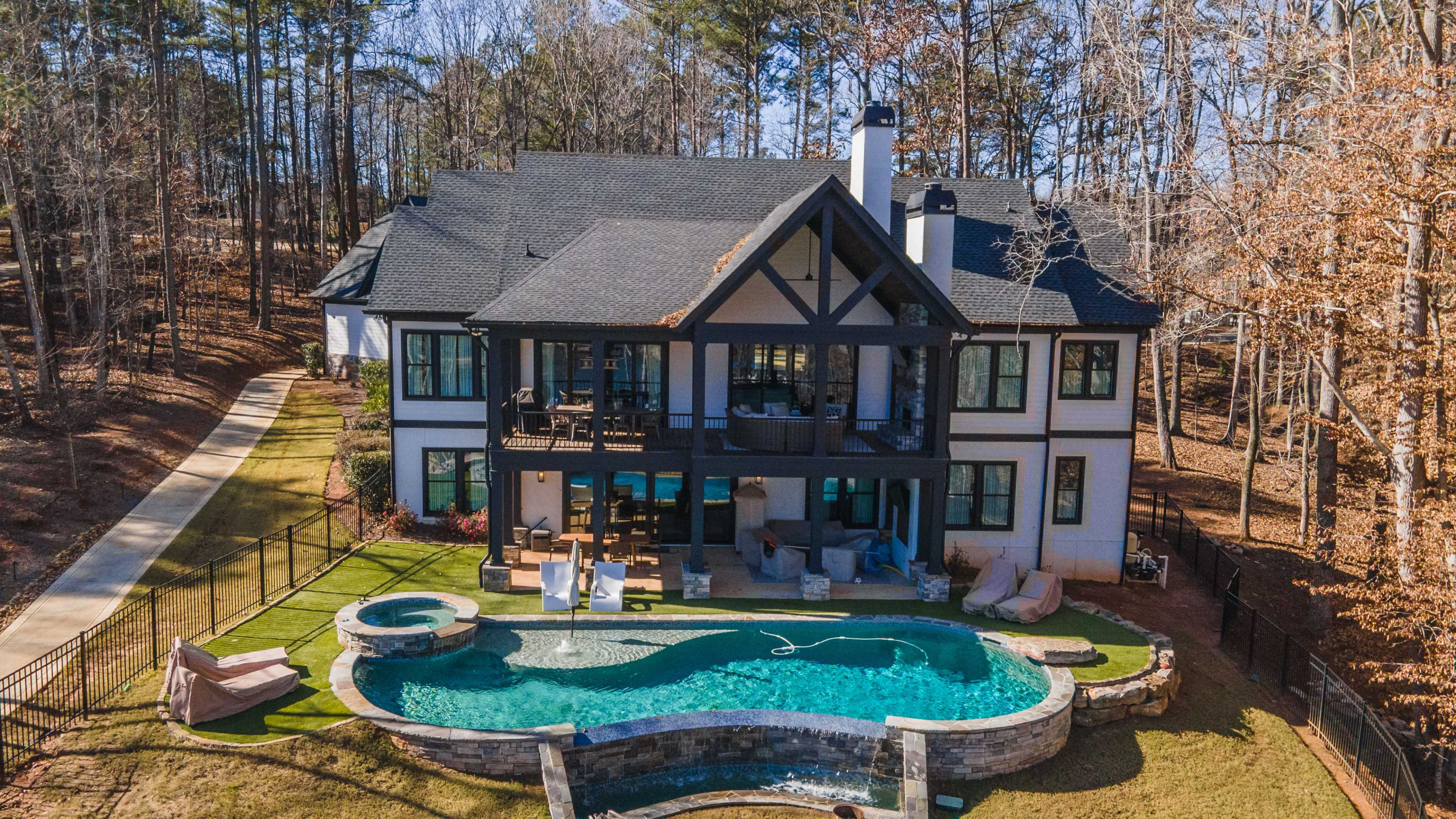 A spacious modern house with a black and white exterior features a pool and hot tub, set in a wooded area.