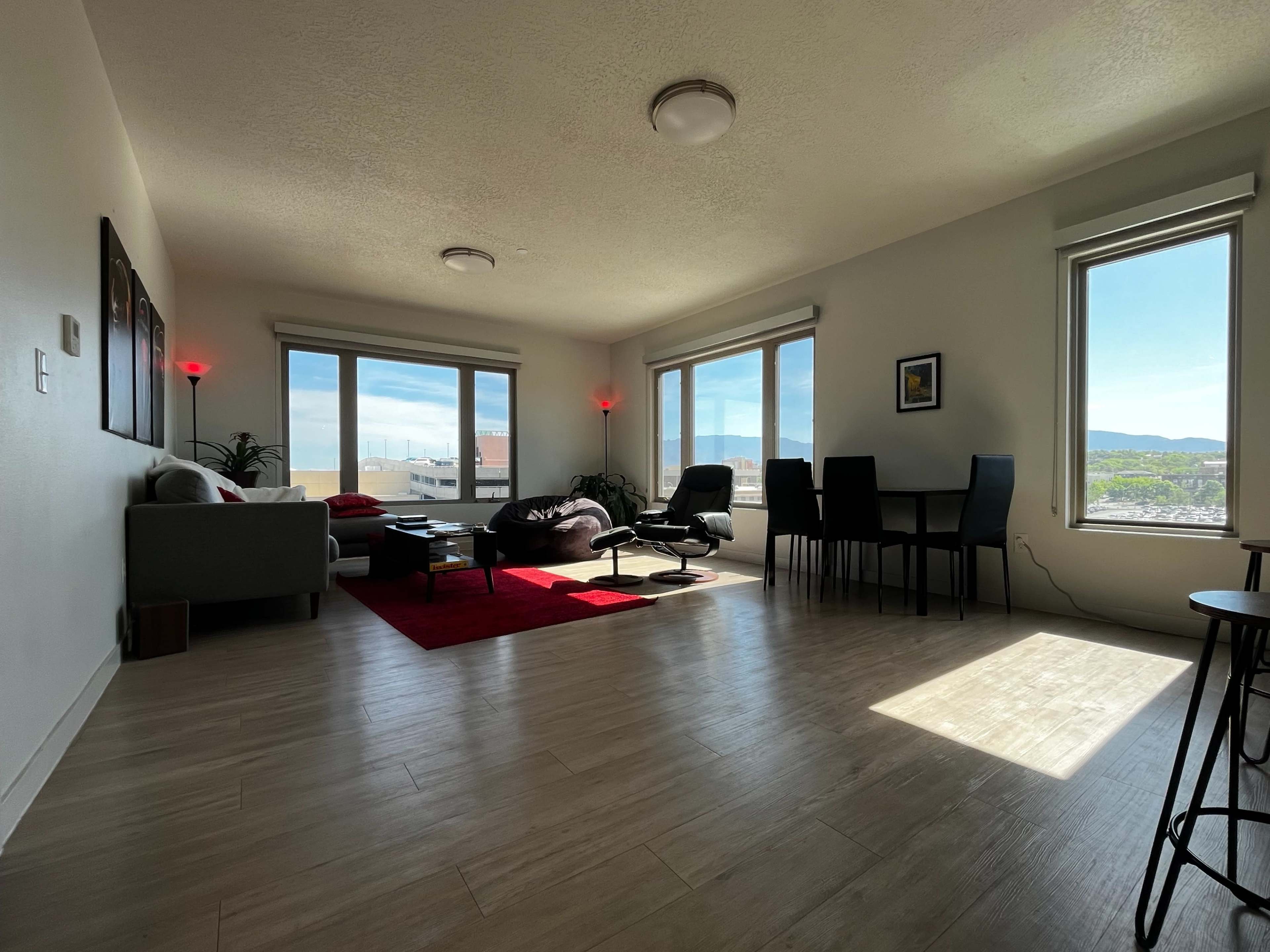 A bright living room with large windows, a sofa, a coffee table, and a dining area, all set against a view of distant mountains.
