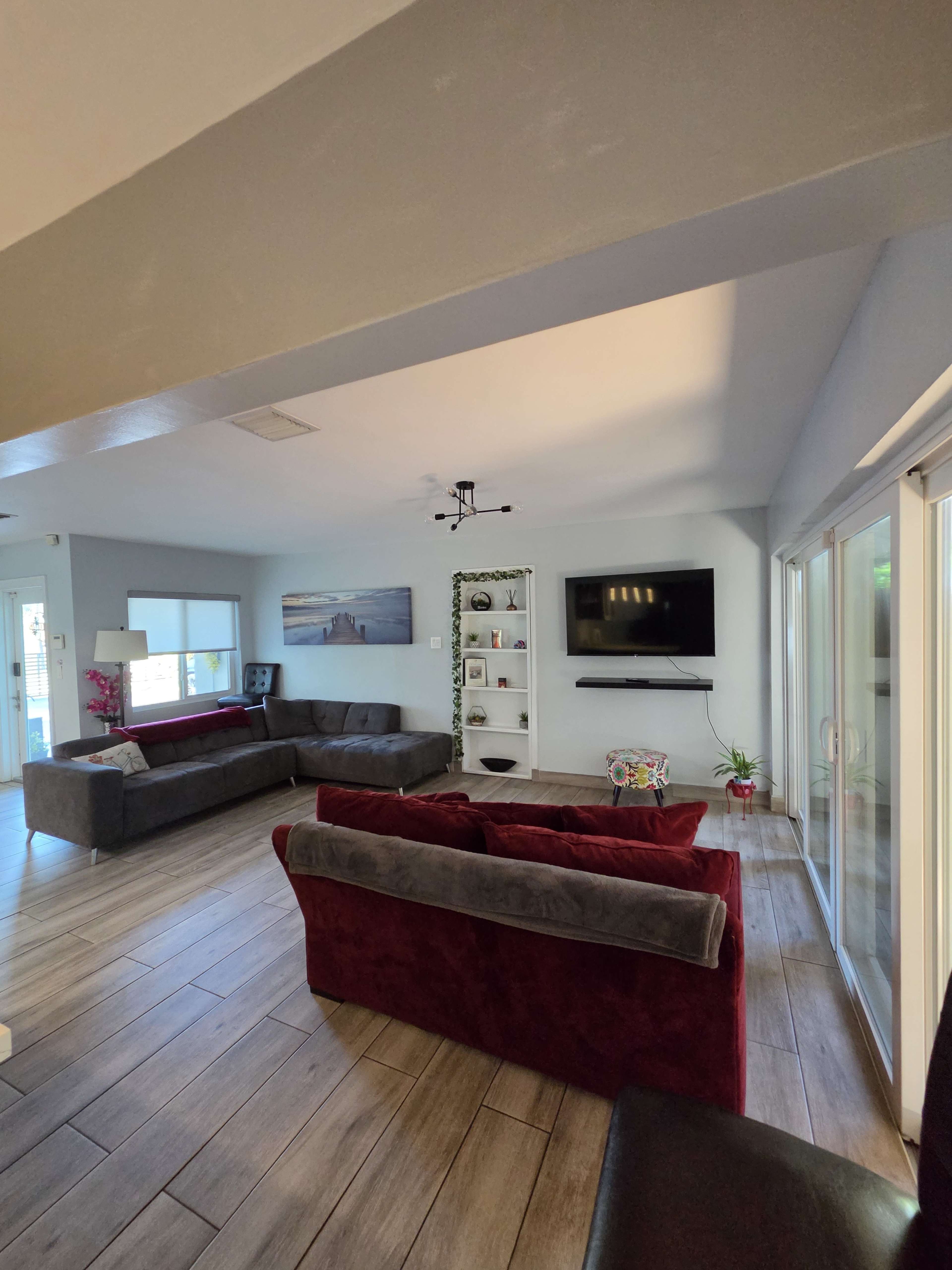 The living room features two sectional sofas facing each other, a mounted television on the wall, and sliding glass doors leading to an outdoor area.