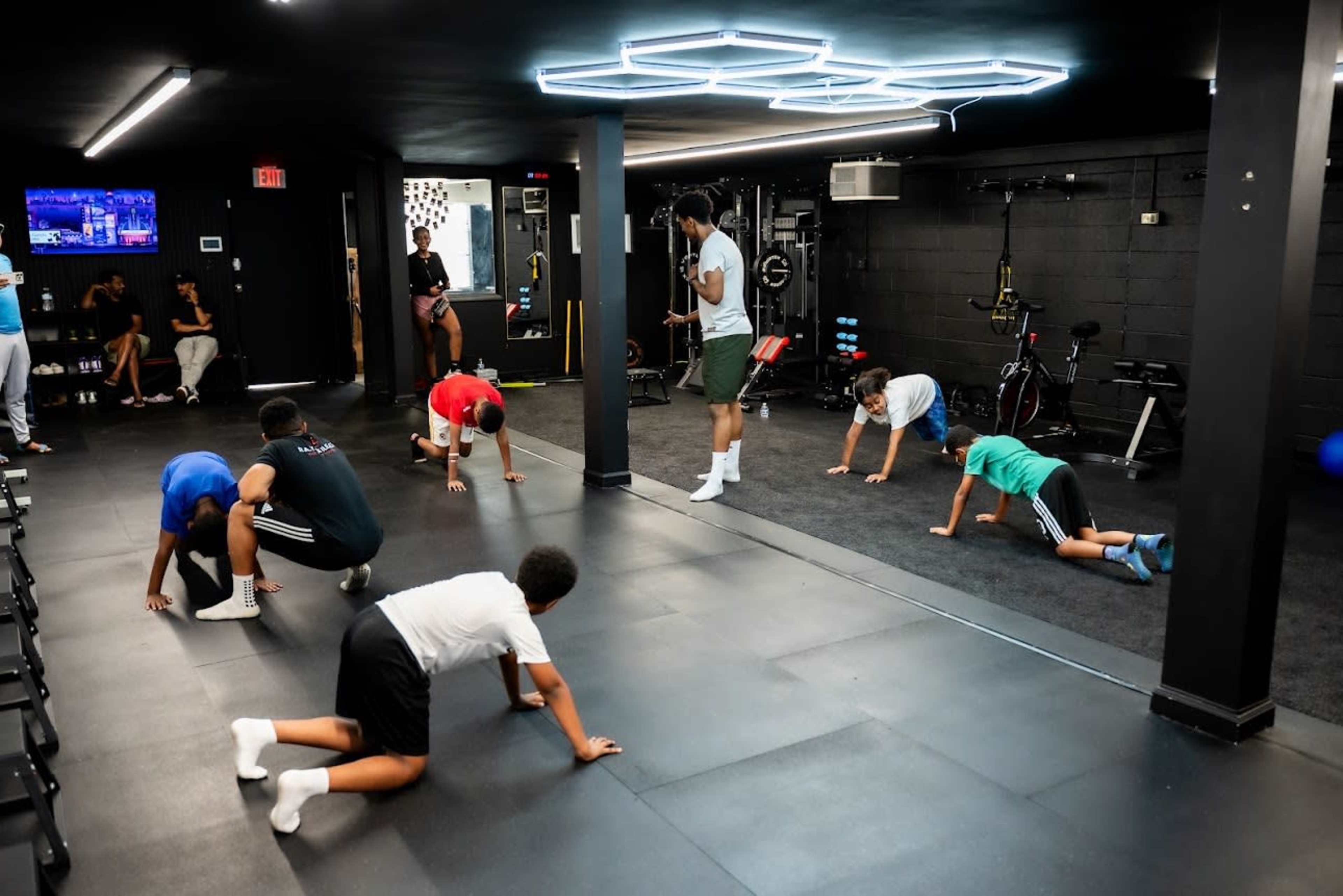 A group of children performs various exercises in a fitness studio while an instructor guides them.