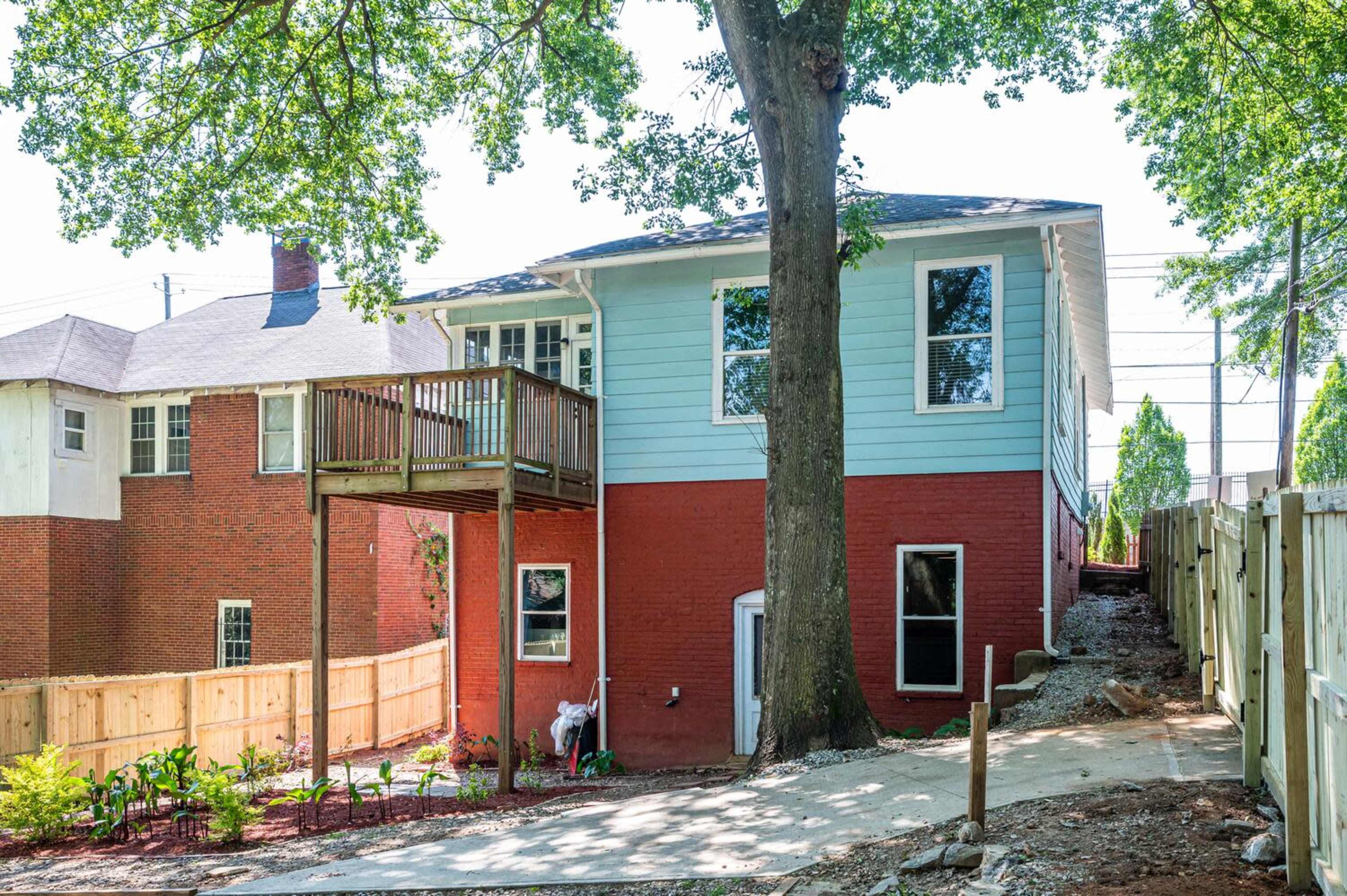 A two-story house with a deck, located beside a yard with landscaping and a protective fence.