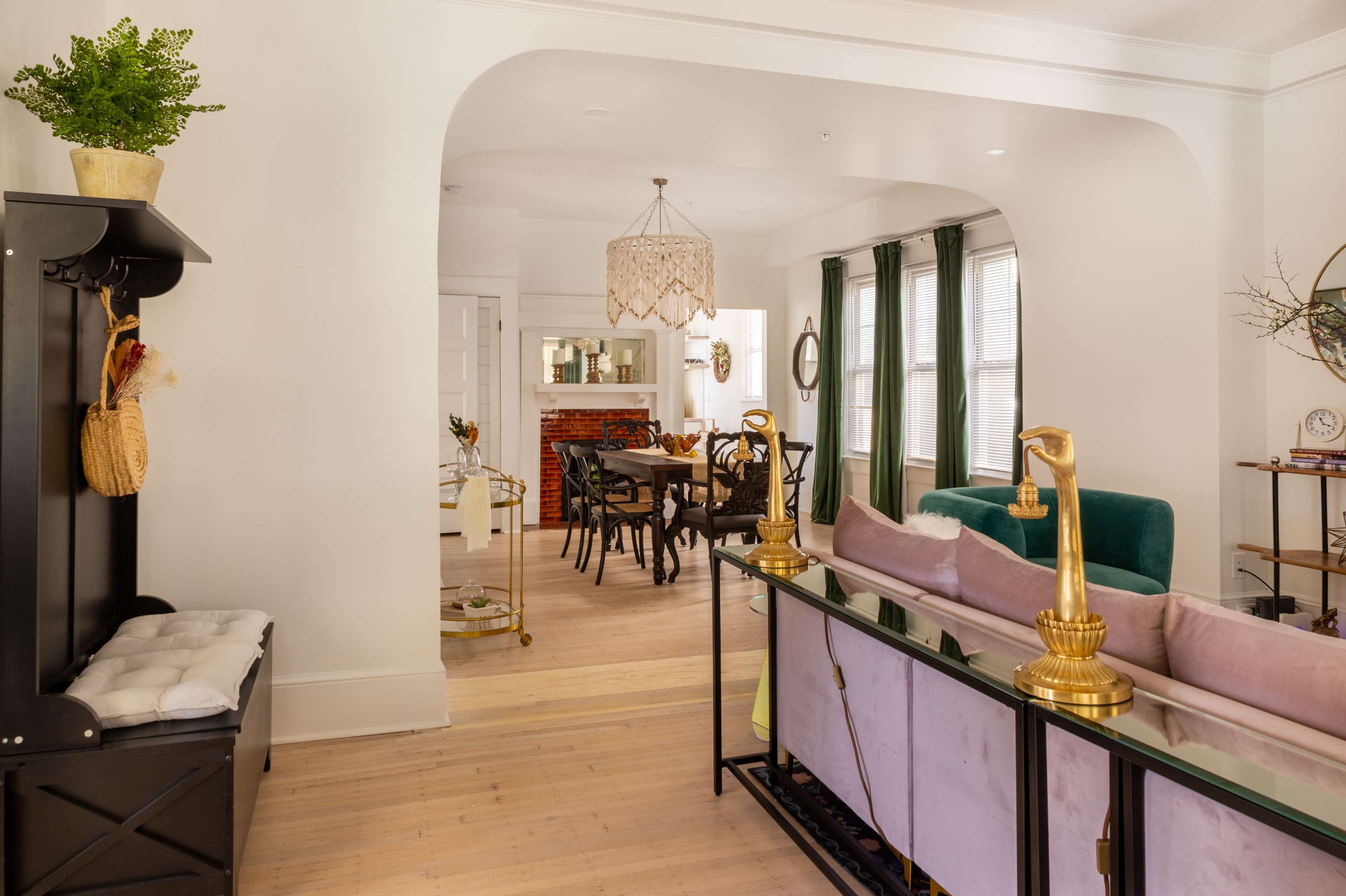 A well-lit, open-concept living and dining area featuring a green sofa, a dining table with black chairs, and a decorative chandelier overhead.