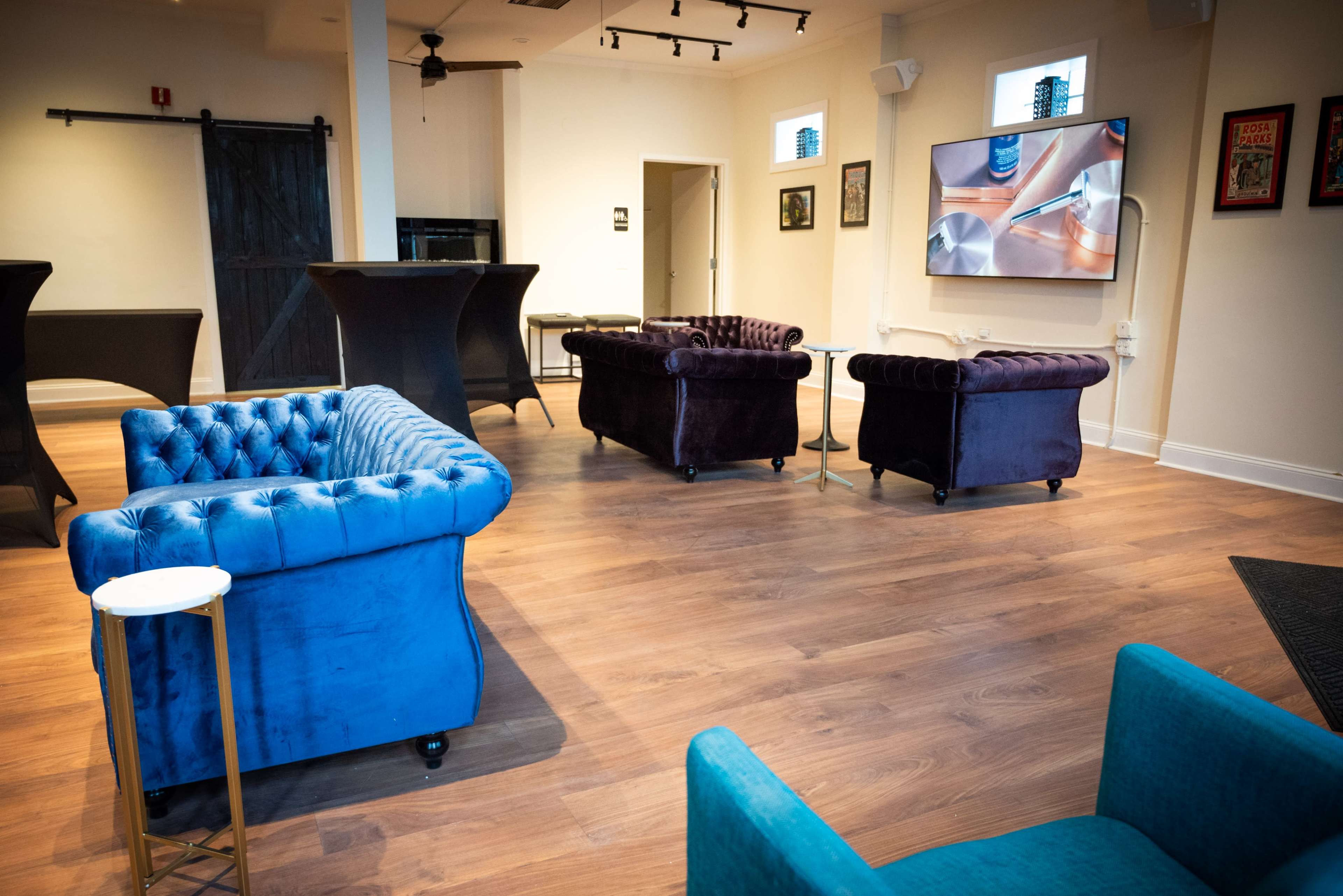 The scene shows a modern lounge area with several tufted couches in varying colors, a television mounted on the wall, and a wooden floor.