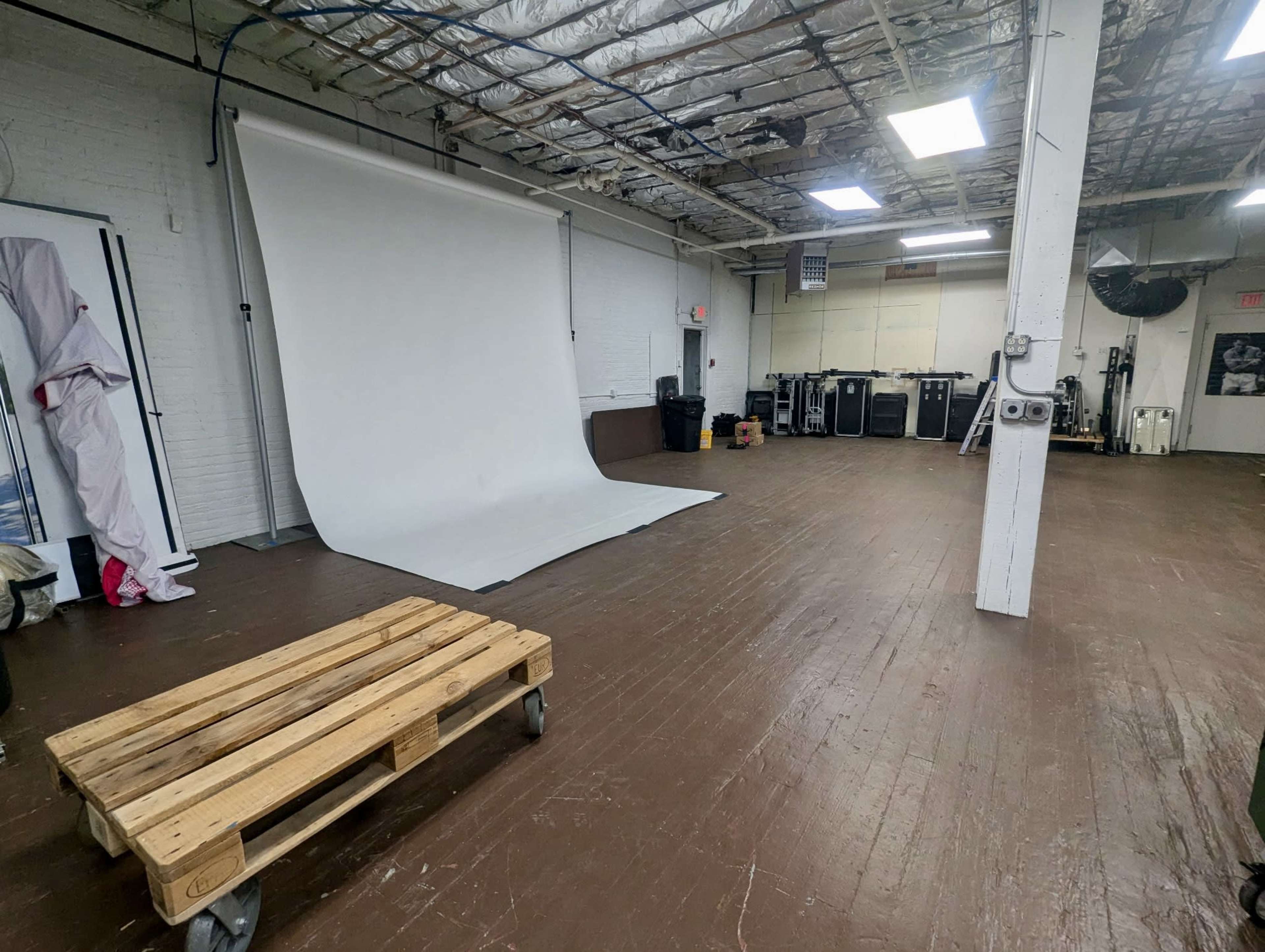A spacious, empty studio features a white backdrop, wooden flooring, and various equipment along the walls.