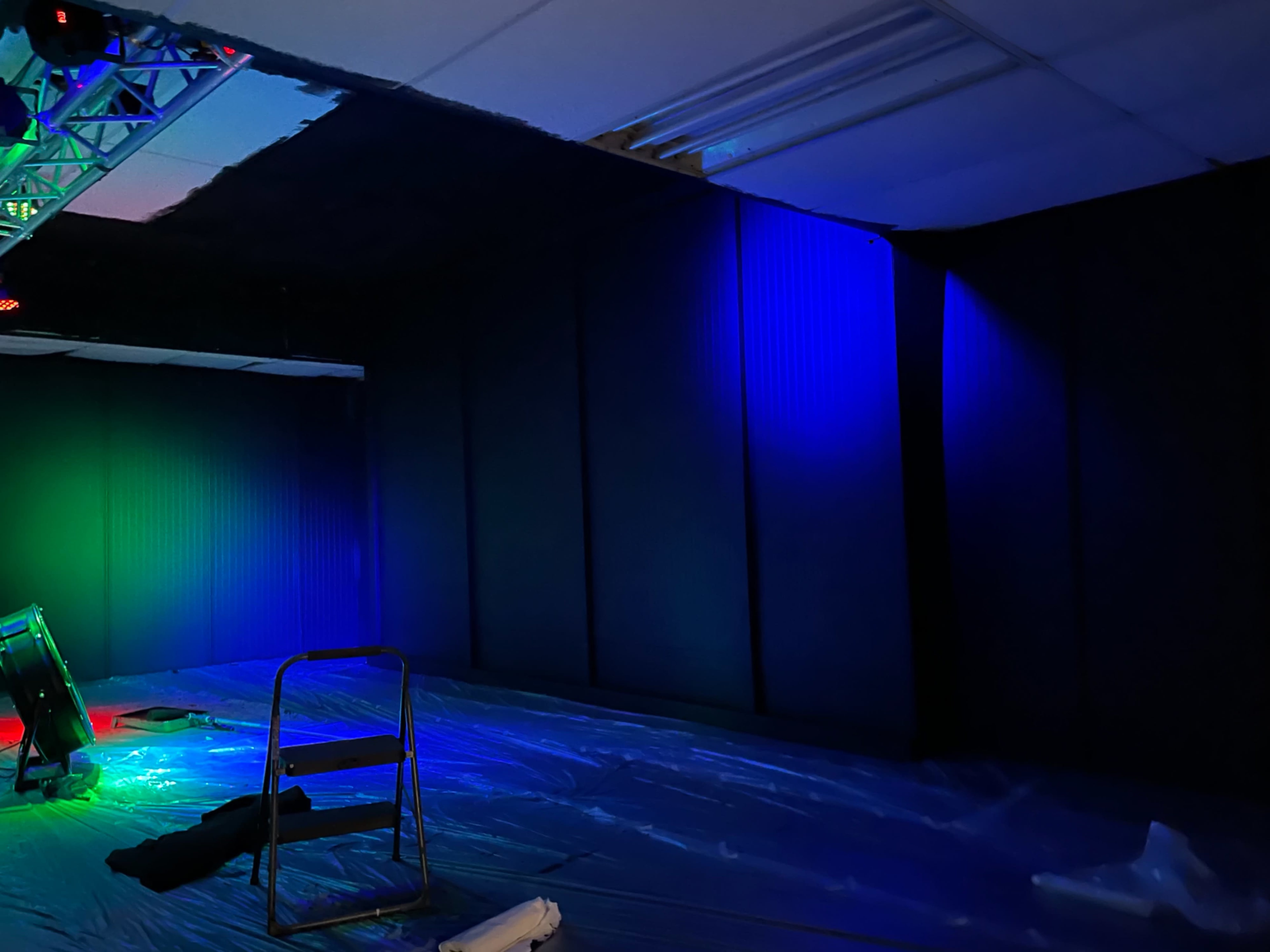 An empty room with dark walls, a partially visible ceiling, and colored lighting effects in one corner.