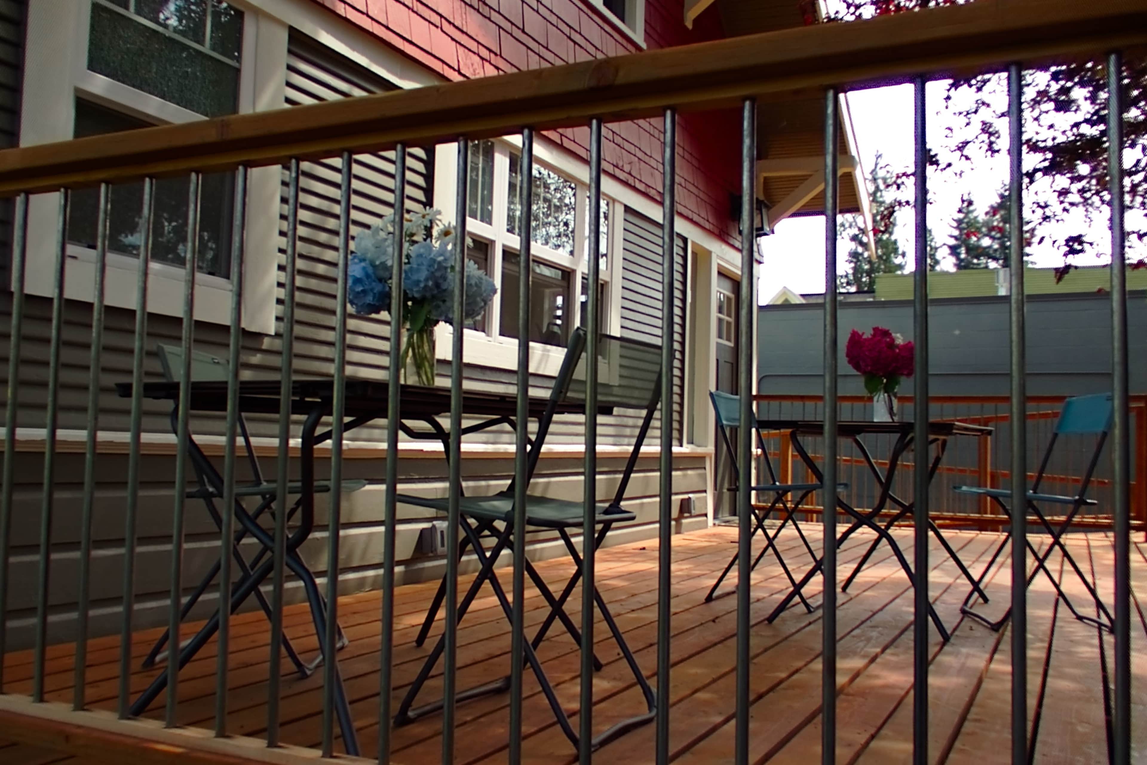 A wooden deck features two tables with vases of flowers and is surrounded by a railing.