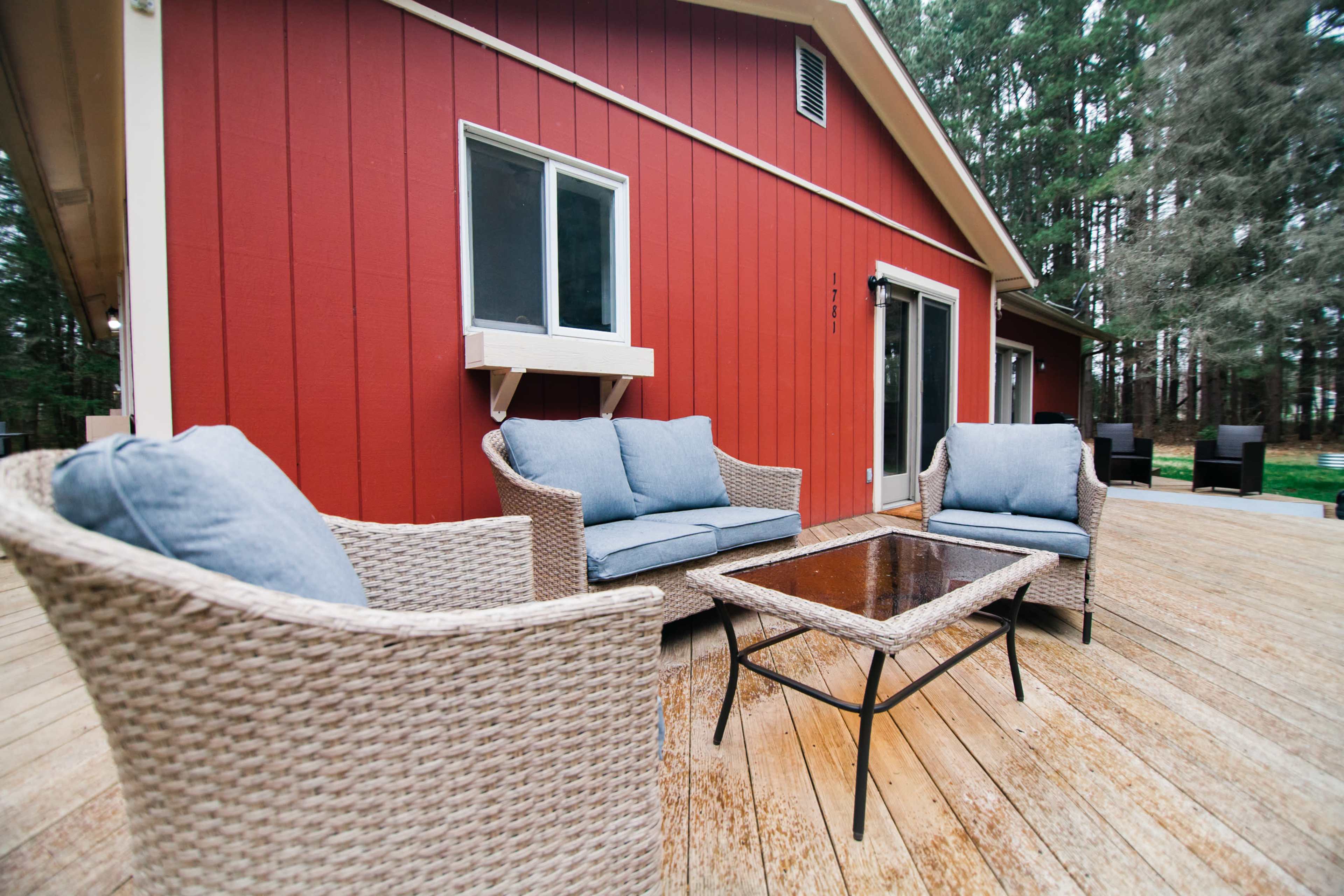 A red house with a wooden deck features two wicker chairs and a glass-top coffee table.