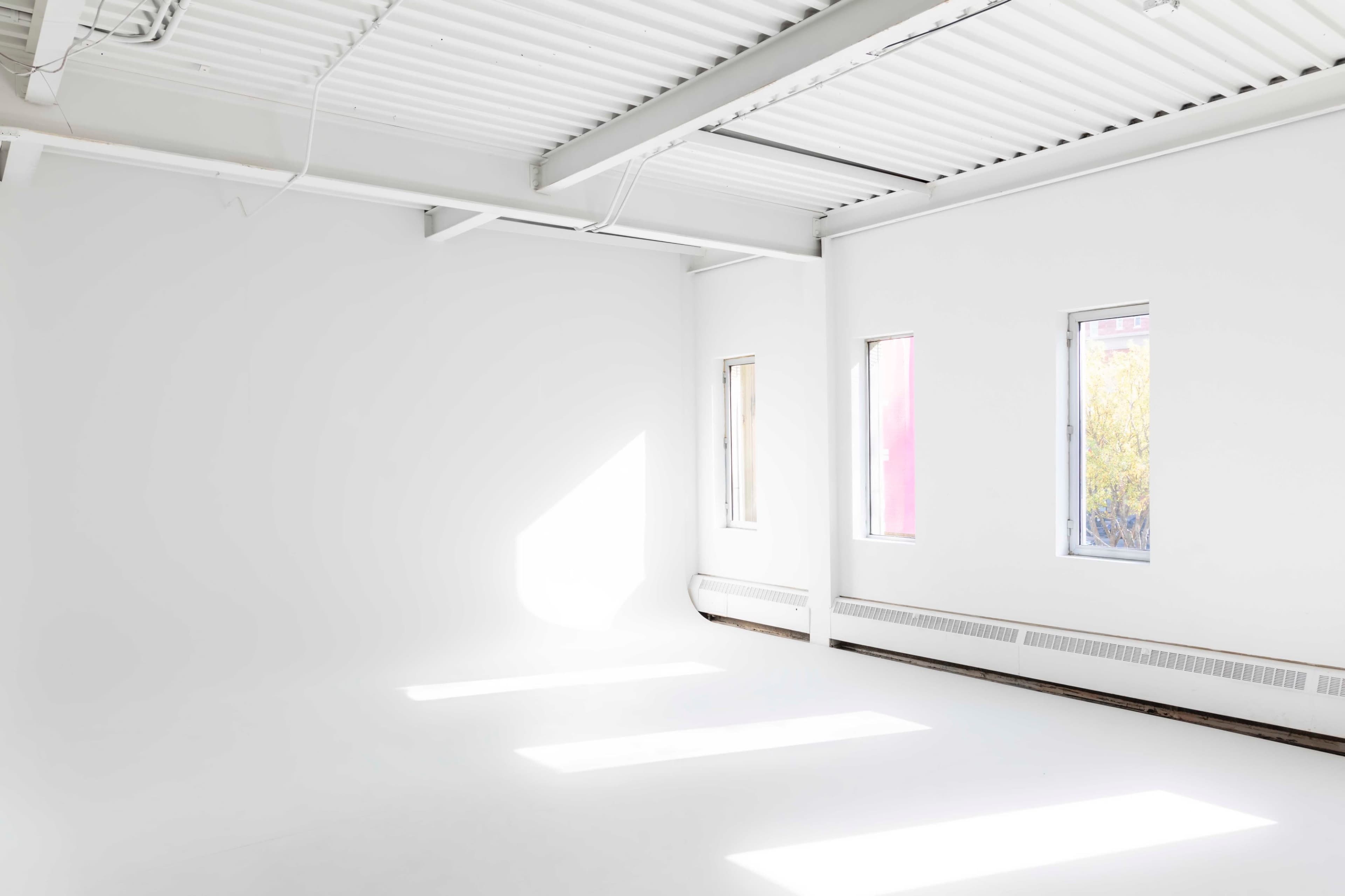 A bright, empty room with white walls and several windows allowing sunlight to fill the space.