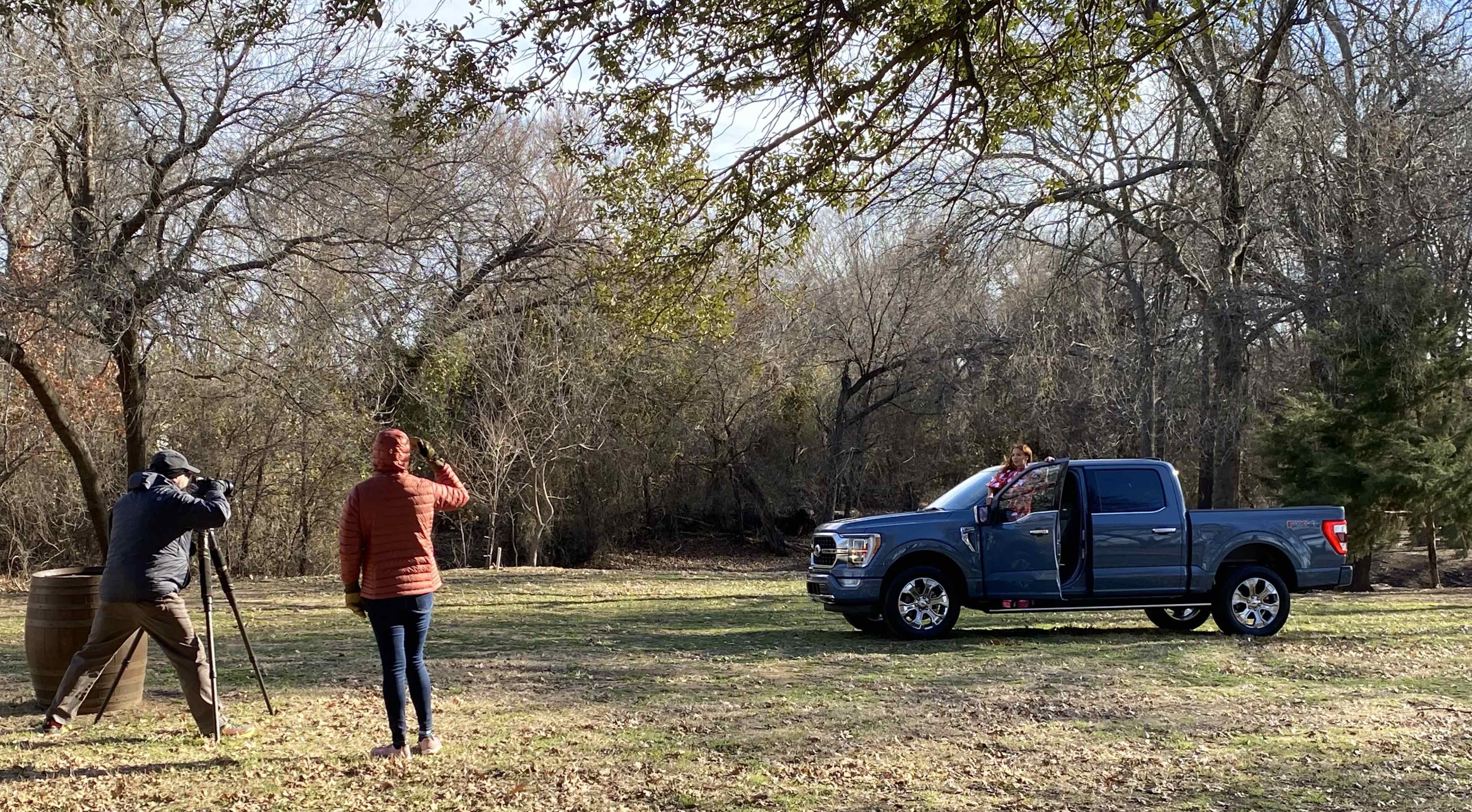 A photographer captures a model posing on the side of a pickup truck in a wooded area.