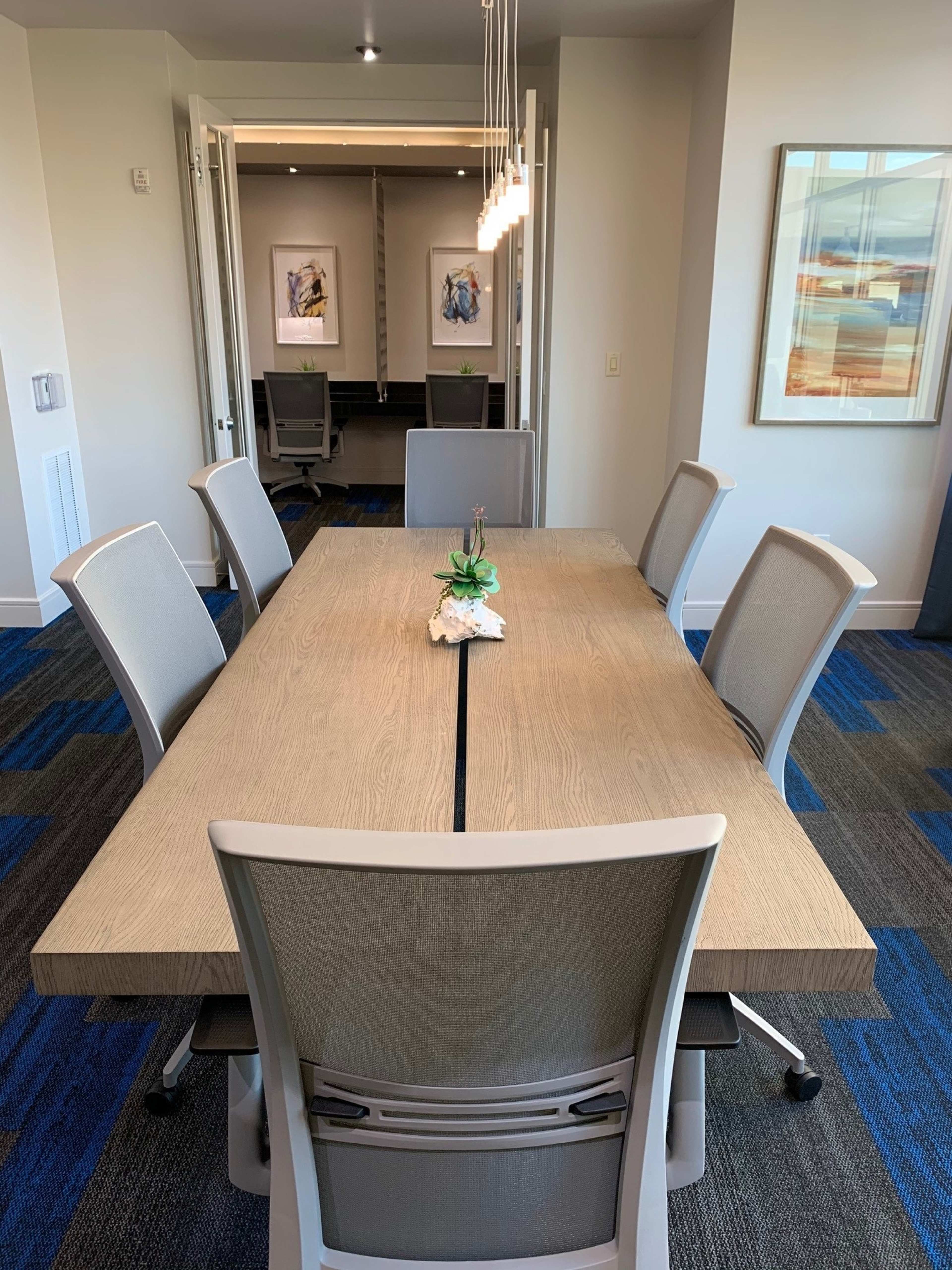 A large conference table is set with six ergonomic chairs in a modern office space, with artwork on the walls and a softly lit atmosphere.