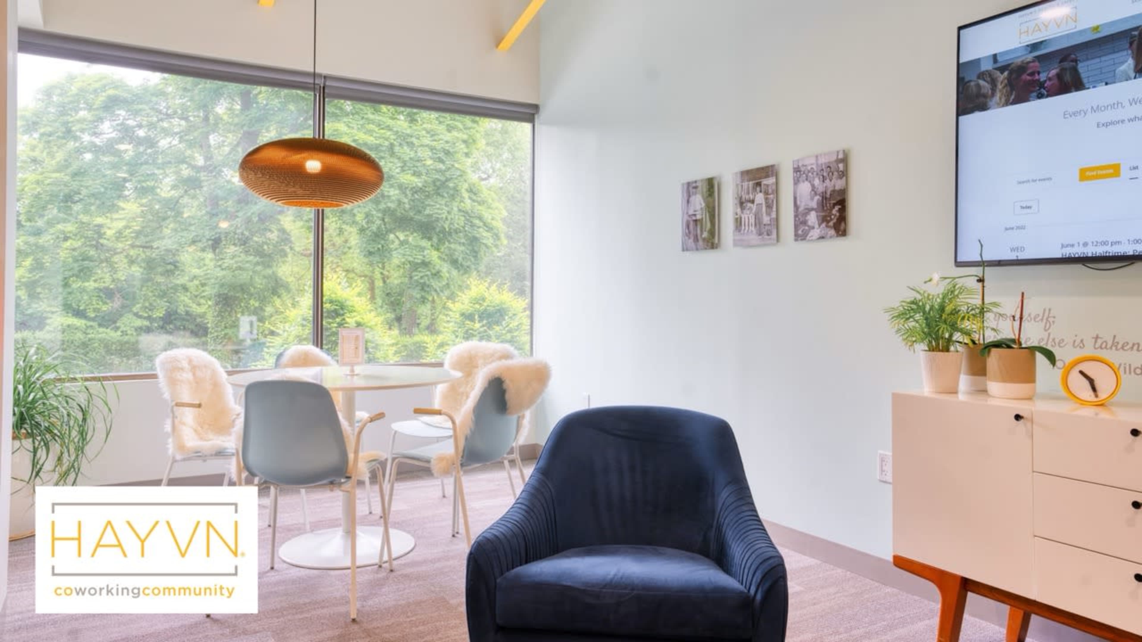 A cozy coworking space features a round table with plush chairs and a large window overlooking greenery.