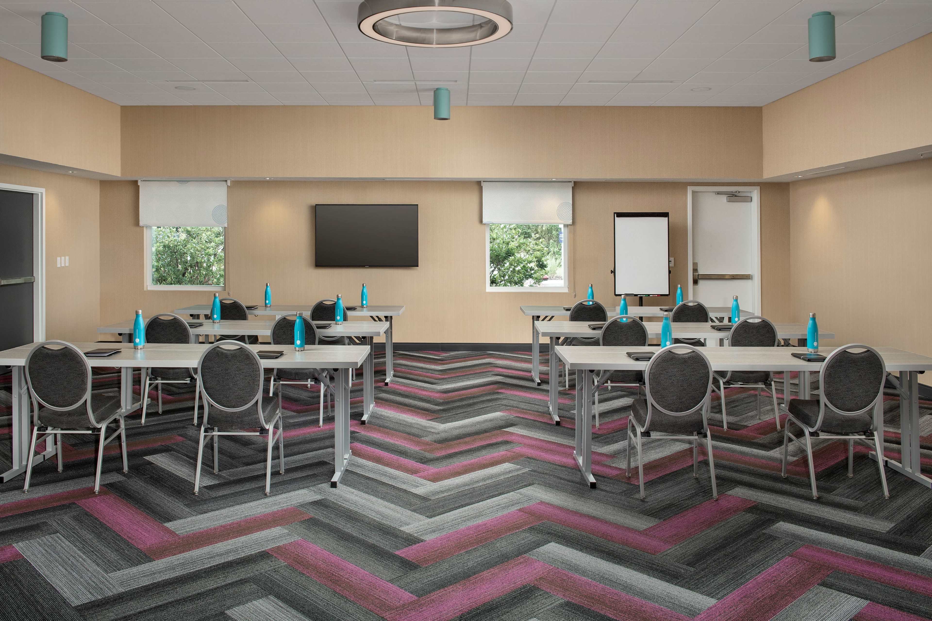 The image shows a modern conference room with a chevron-patterned carpet, multiple tables arranged for a meeting, and bright blue water bottles on each table.
