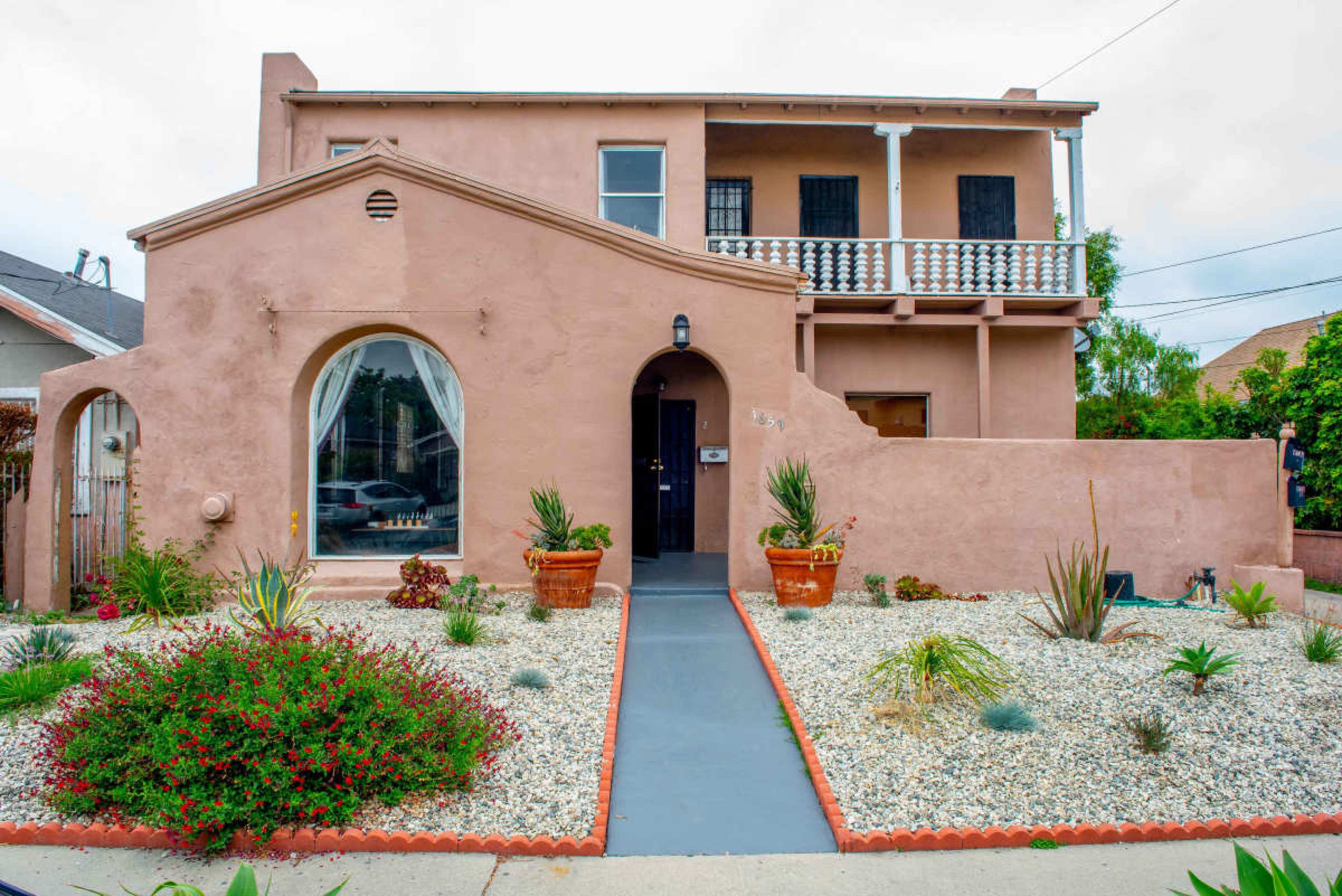 A two-story pink stucco house features a landscaped front yard with gravel and potted plants.