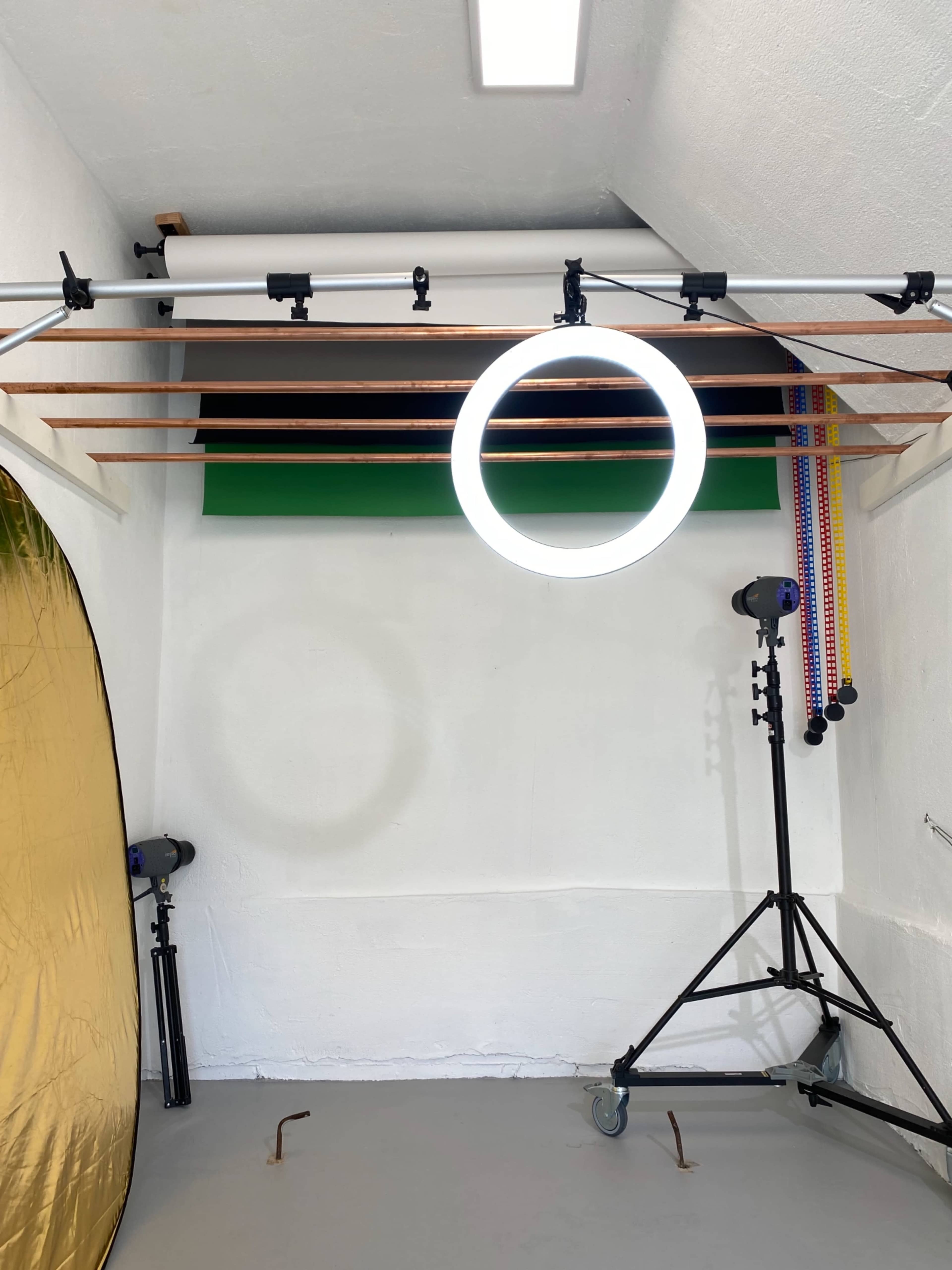 A photography studio with a circular light fixture, backdrop supports, and a rolling stand.