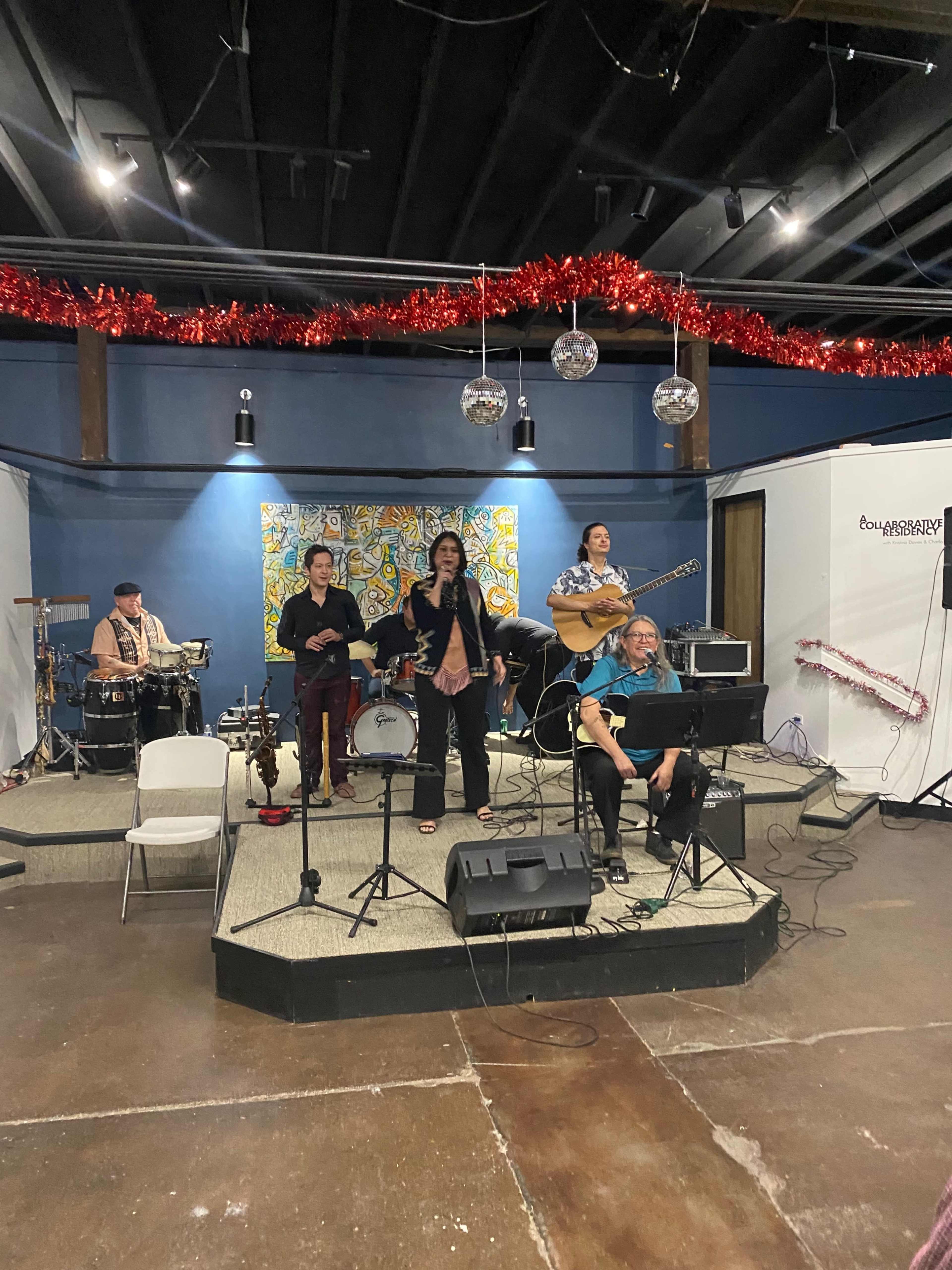 A group of musicians performs on a small stage adorned with decorative tinsel and disco balls.
