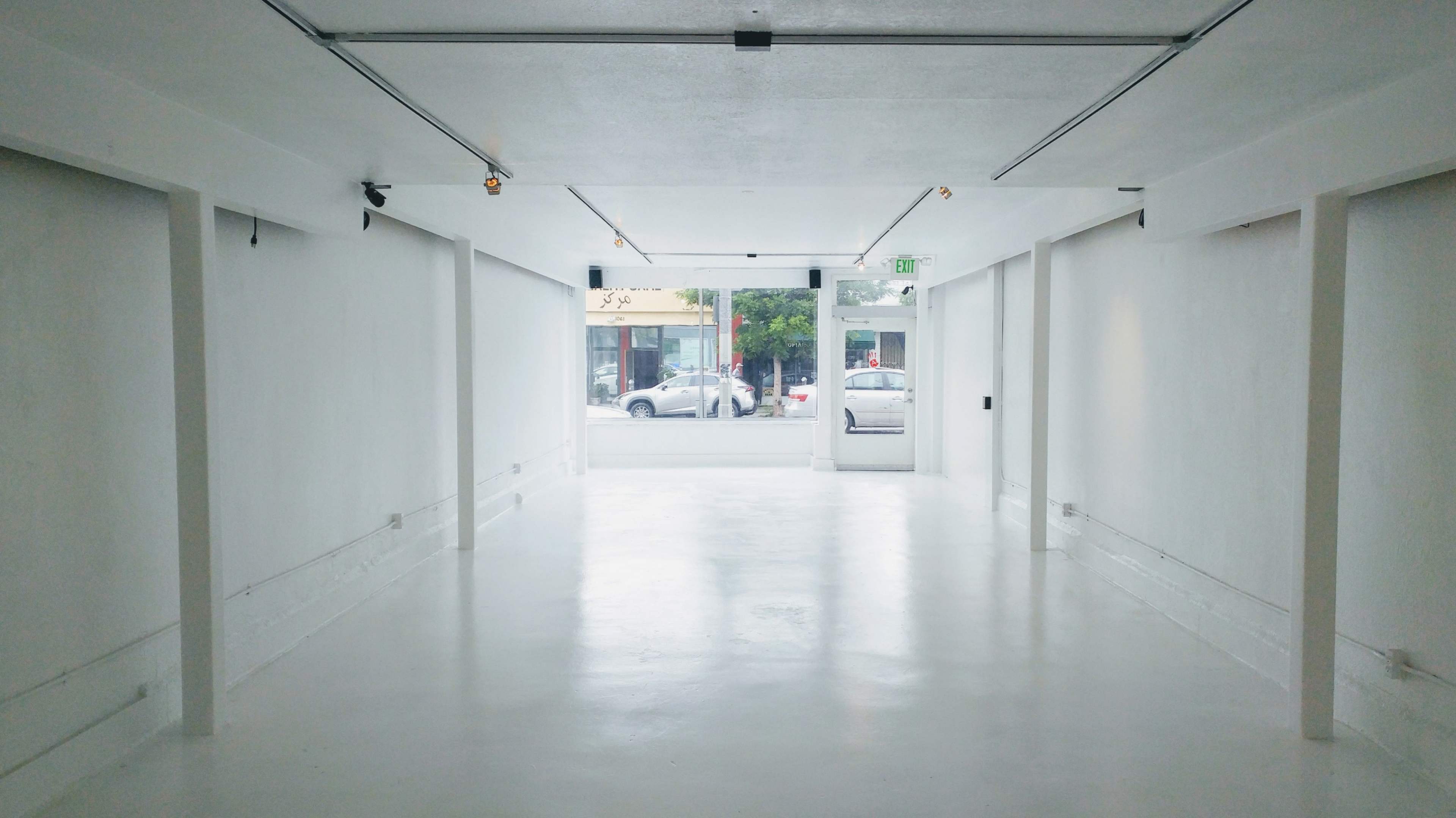 The image shows a bright, empty corridor with white walls and a door at the end leading to a street.