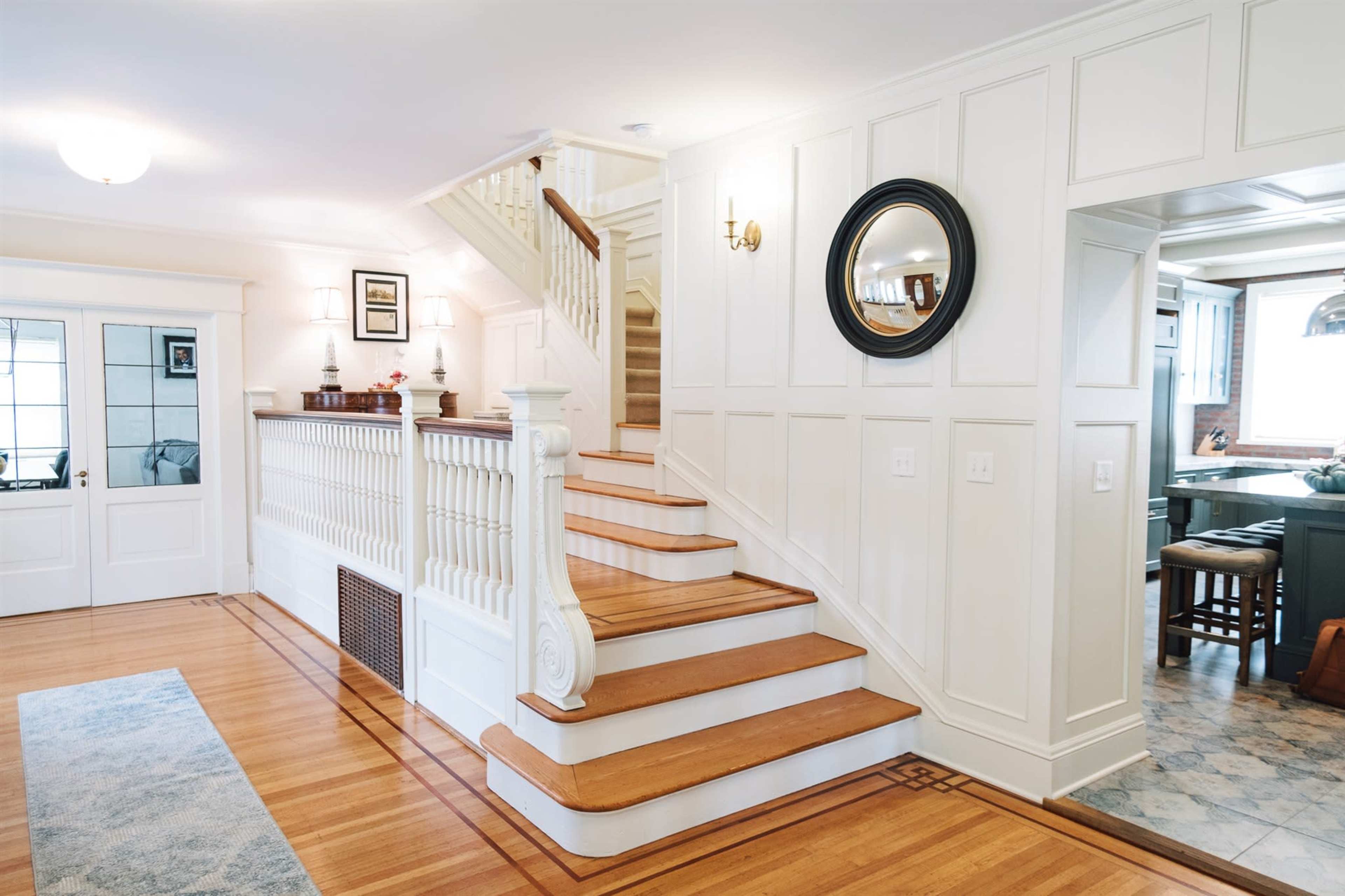 The image shows an interior view of a home featuring a staircase with wooden steps, white paneling on the walls, and a small landing area adjacent to a kitchen.