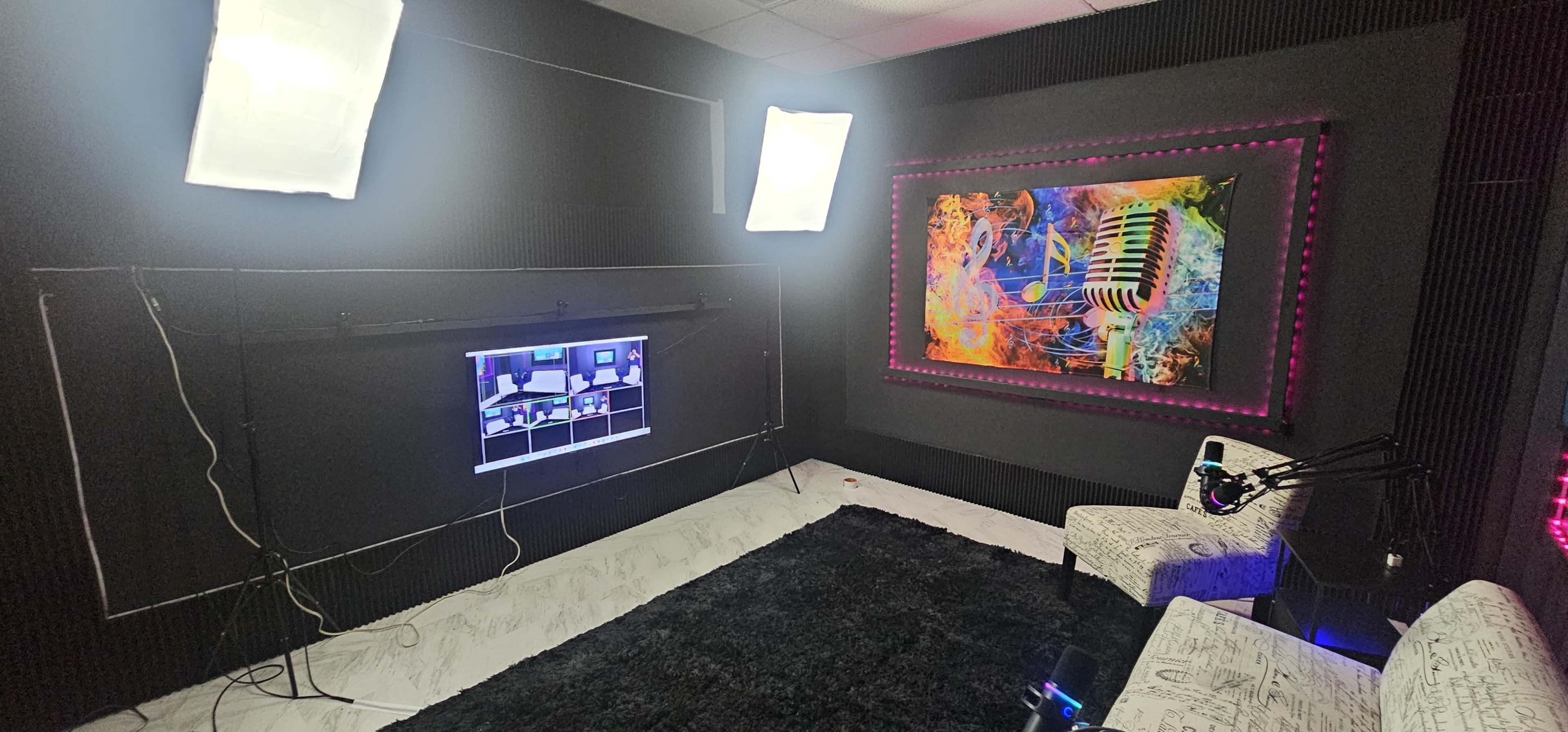 The image shows a modern recording studio equipped with soft lighting, a large colorful mural, and a seating area with microphones and a monitor display.