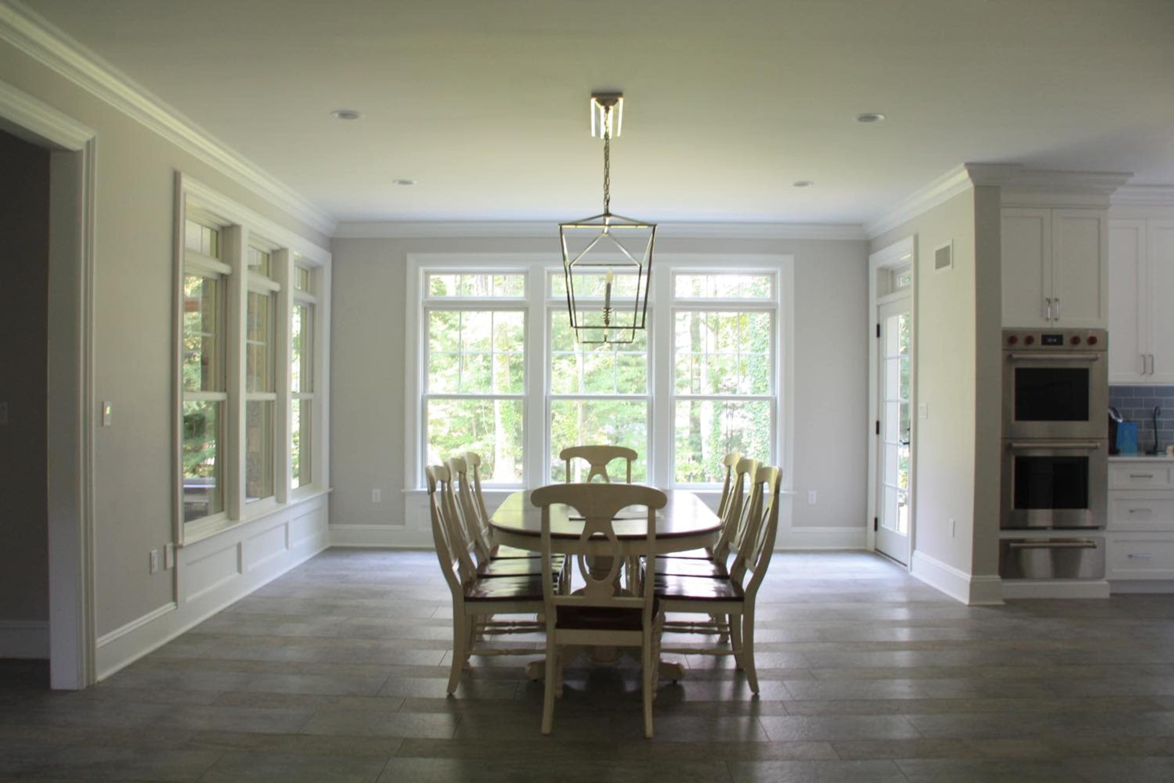 A spacious kitchen features a large wooden dining table surrounded by white chairs, with several large windows allowing natural light to fill the space.