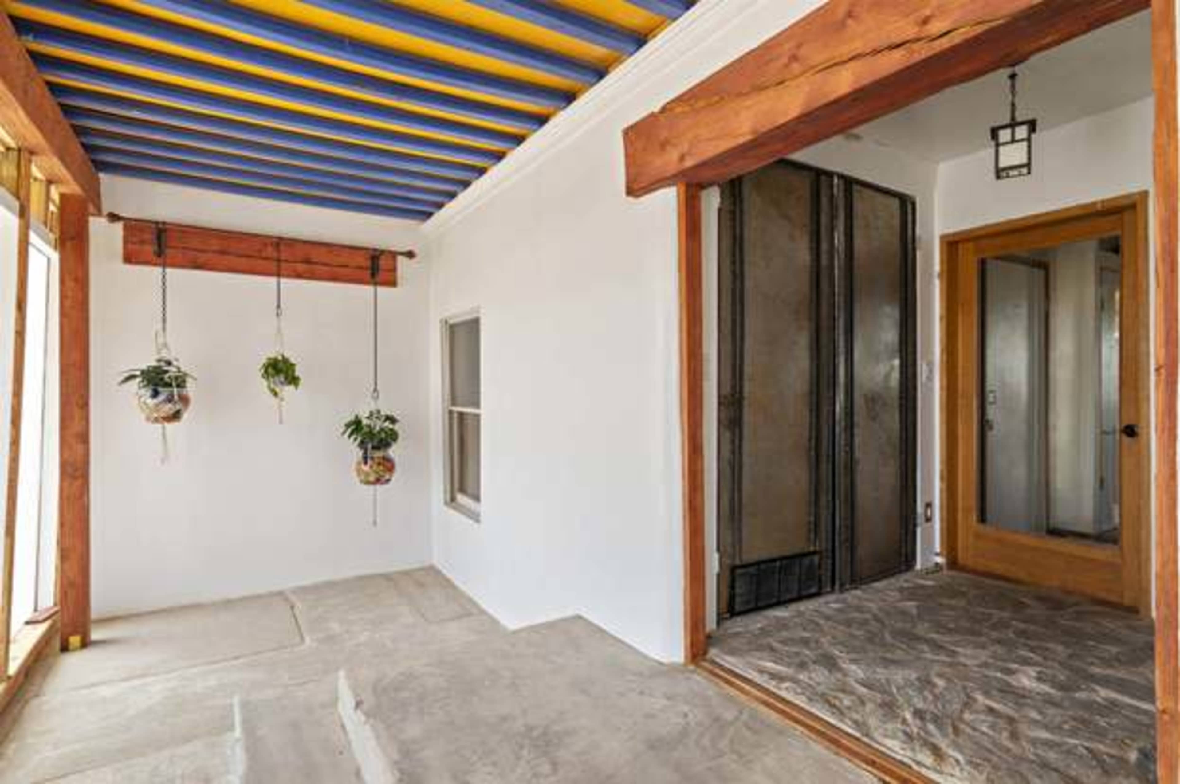 A porch with a colorful striped ceiling, hanging plants, and a doorway leading into a room with slate flooring.
