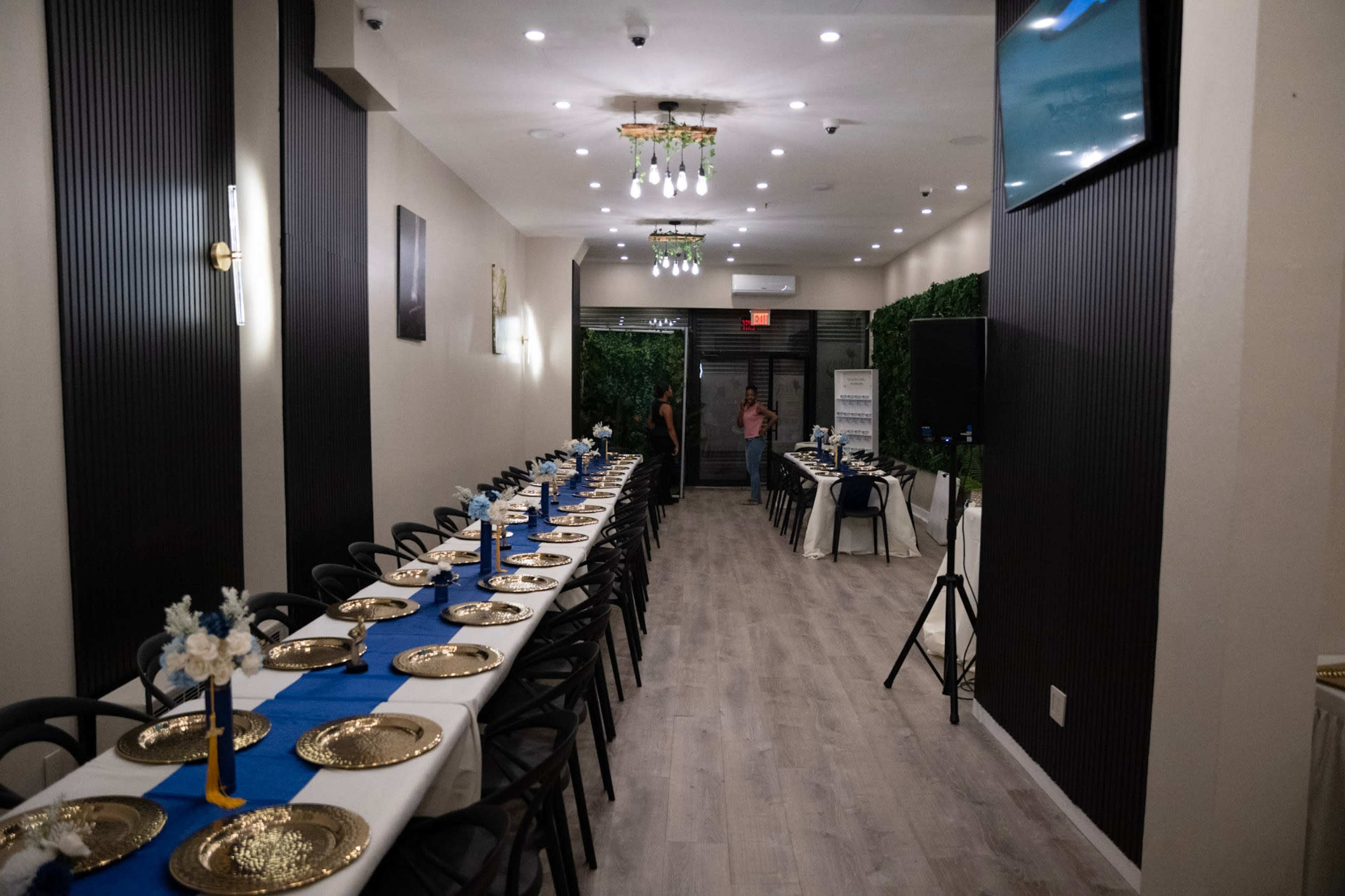 The image shows a long, elegantly set dining table with gold plates and blue table runners in a well-lit restaurant interior.