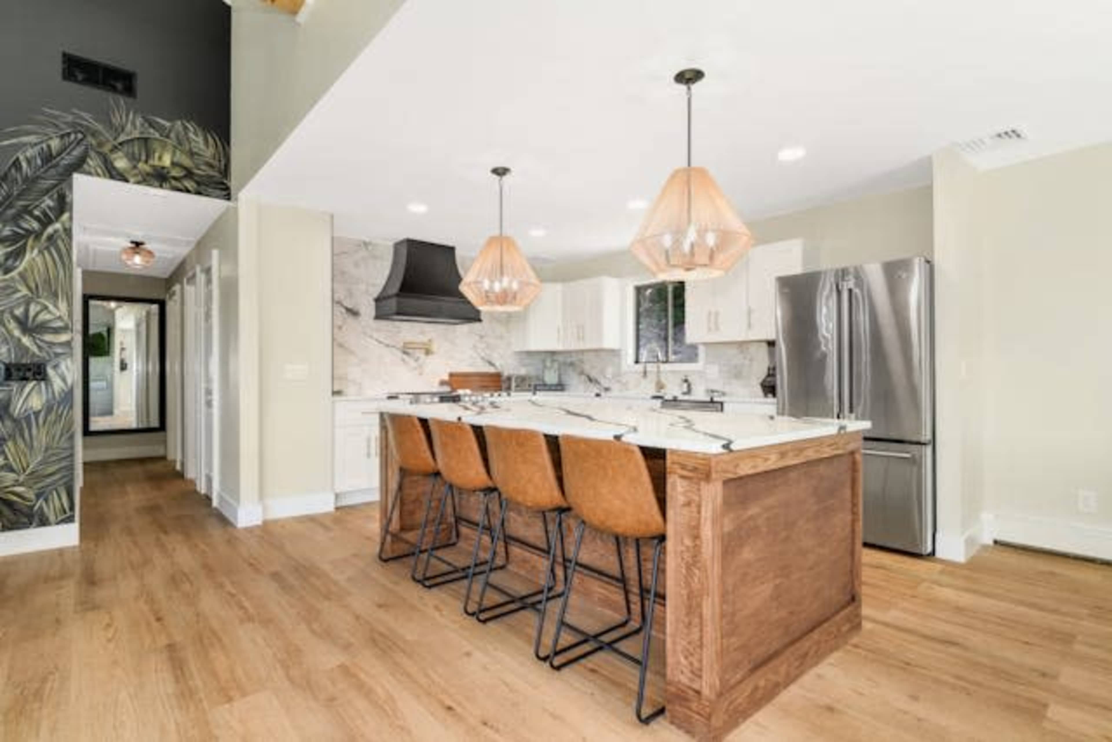 The image shows a modern kitchen with a large island featuring bar stools, pendant lighting, and marble countertops.