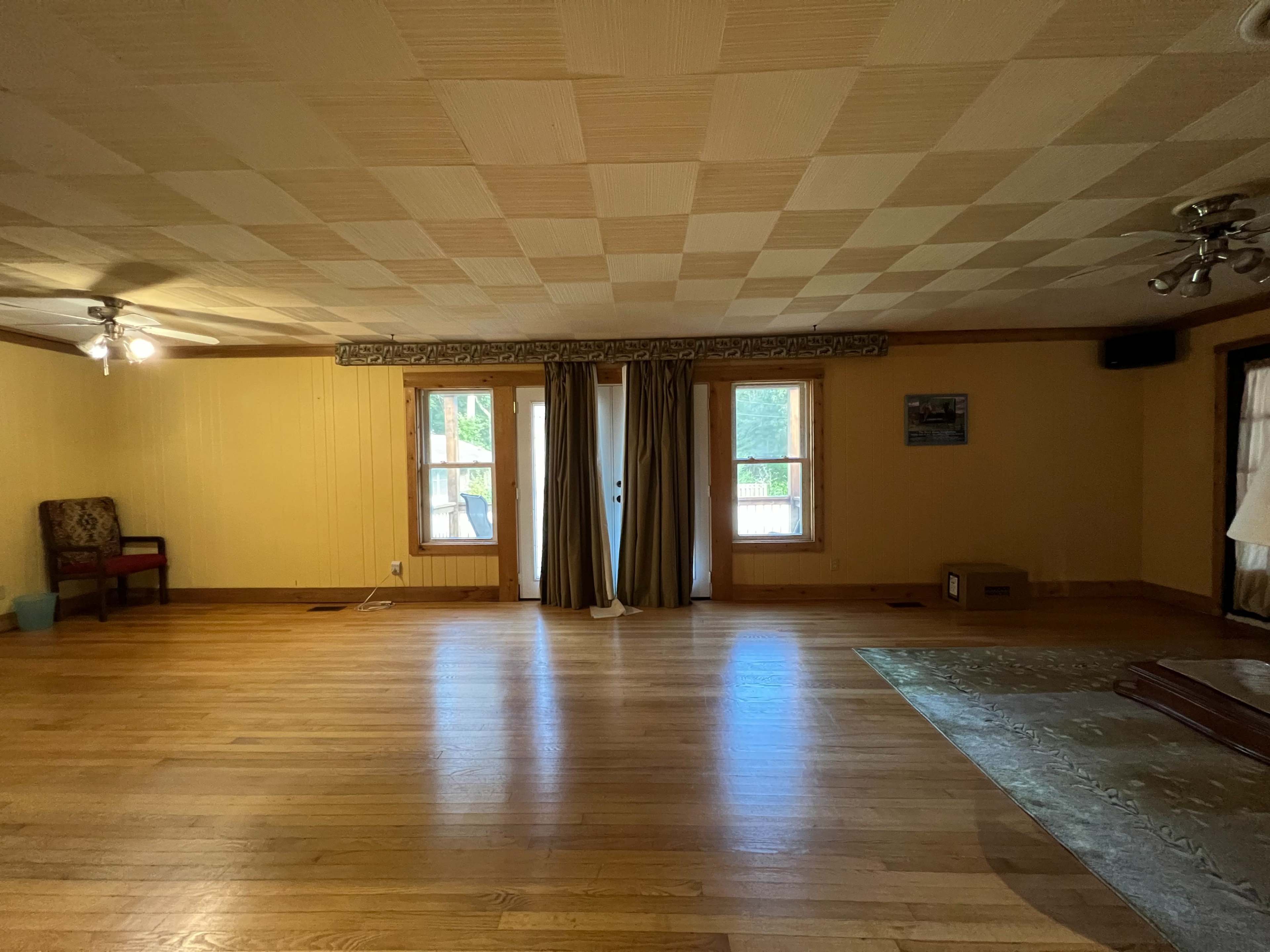 A large, empty room with wooden floors, two windows, and a set of curtains.