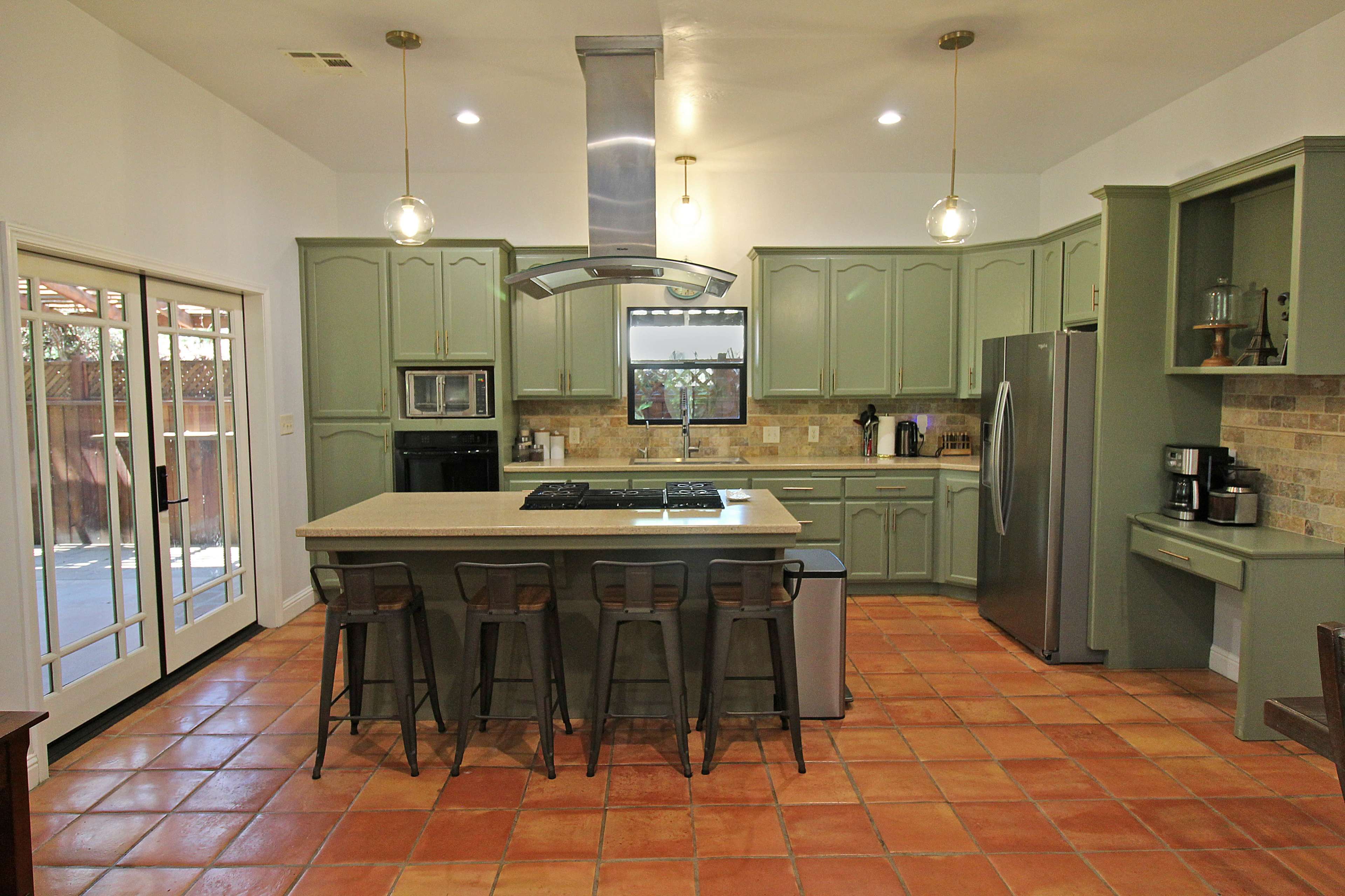 A spacious kitchen with green cabinetry, a large island with bar stools, and a window overlooking an outdoor area.