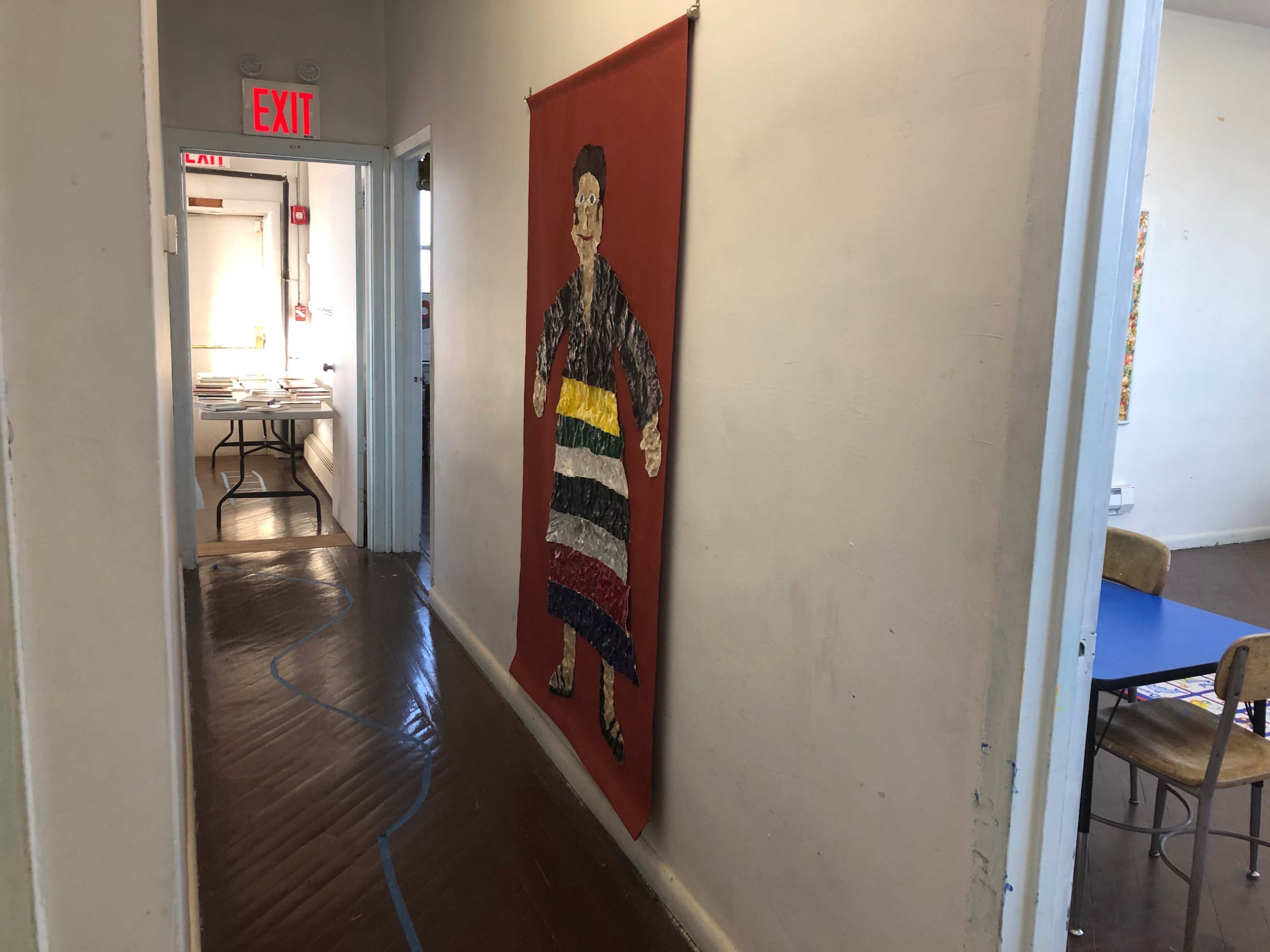 A colorful fabric mural of a figure stands on the wall of a hallway leading to an exit.