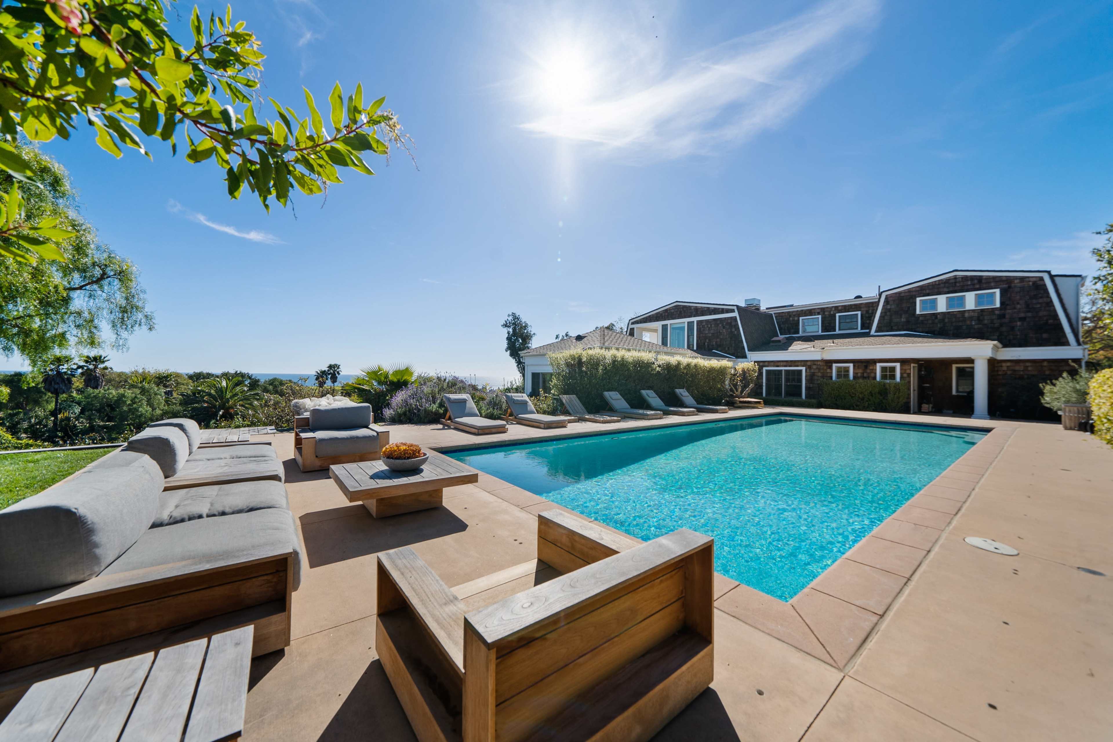 A modern outdoor area features a swimming pool surrounded by lounge chairs and wooden seating against a clear sky.