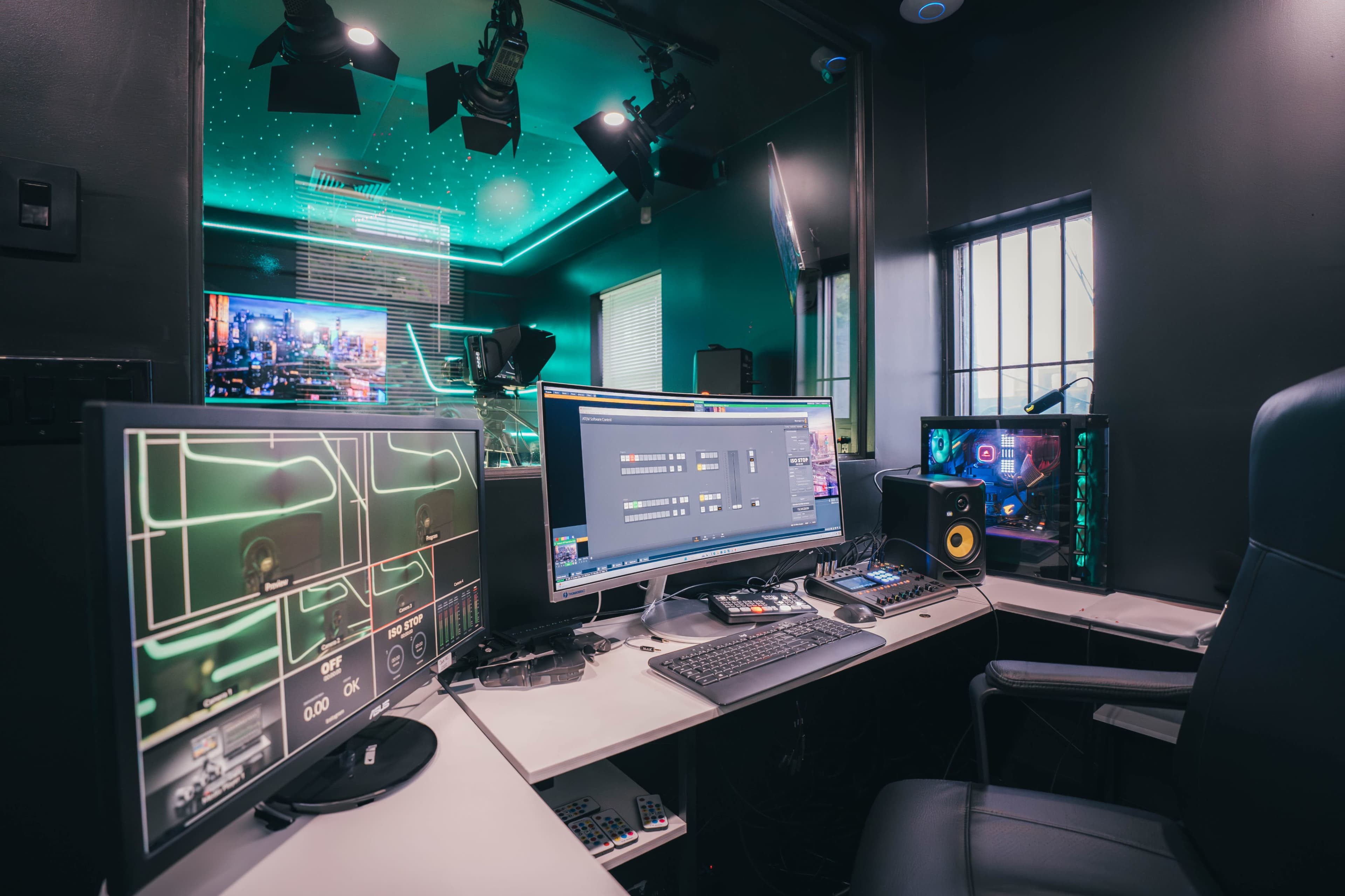 A modern media production workspace with multiple monitors, a keyboard, and a computer setup in a dimly lit room.