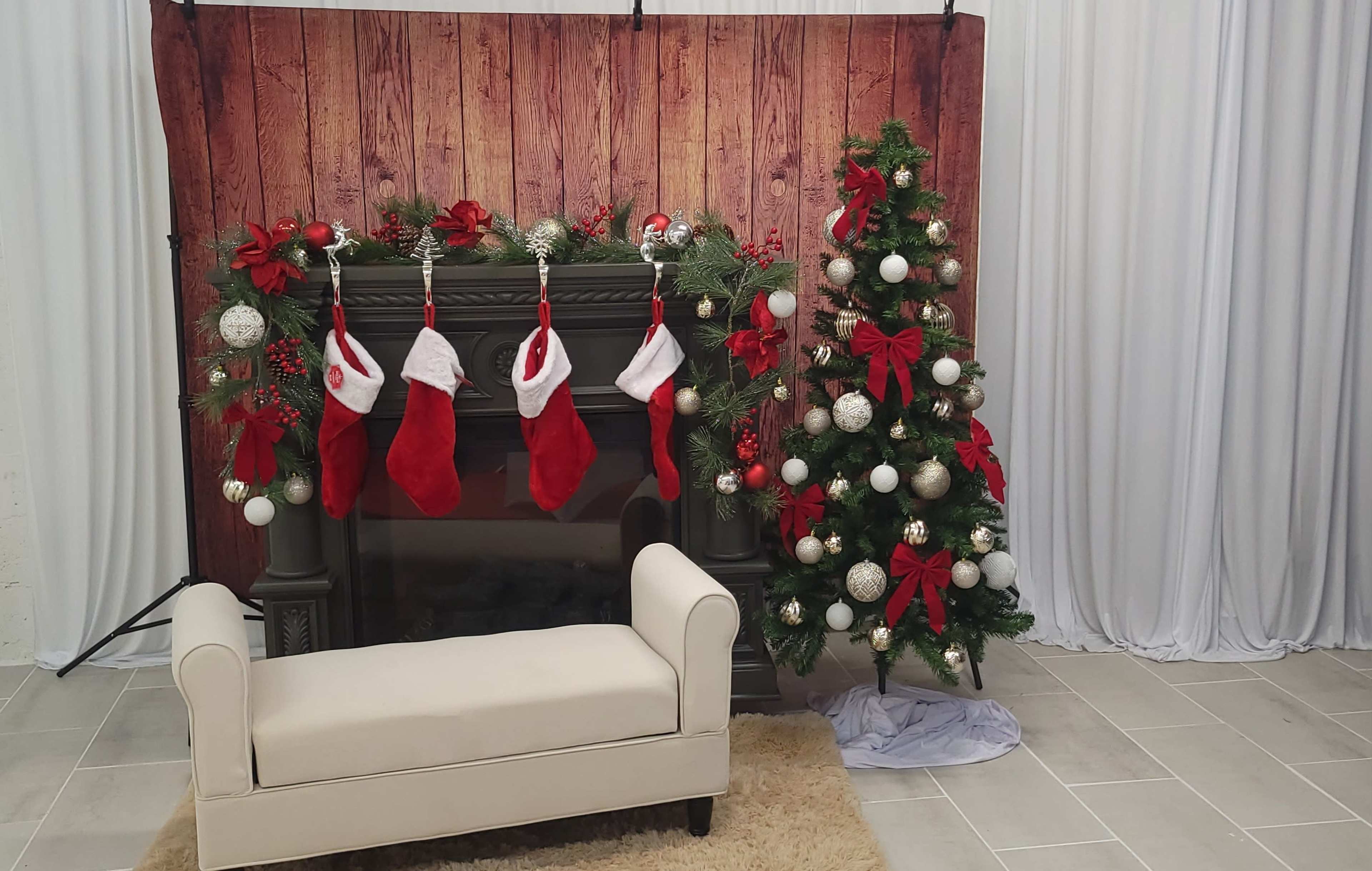 A decorated fireplace with stockings hanging from the mantel, accompanied by a Christmas tree adorned with red bows and ornaments.