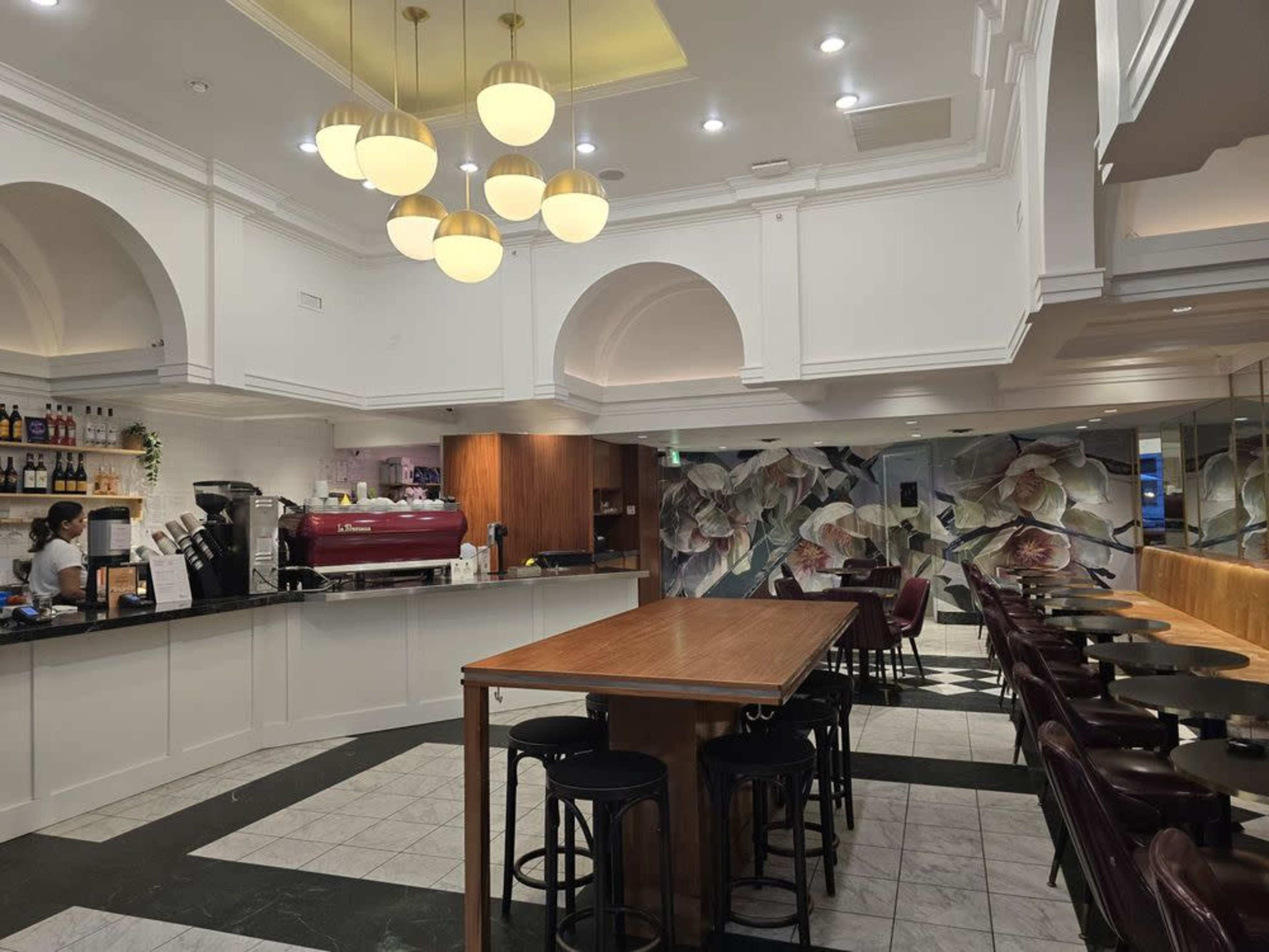The image shows the interior of a café featuring a bar counter, tables, and decorative wall art.