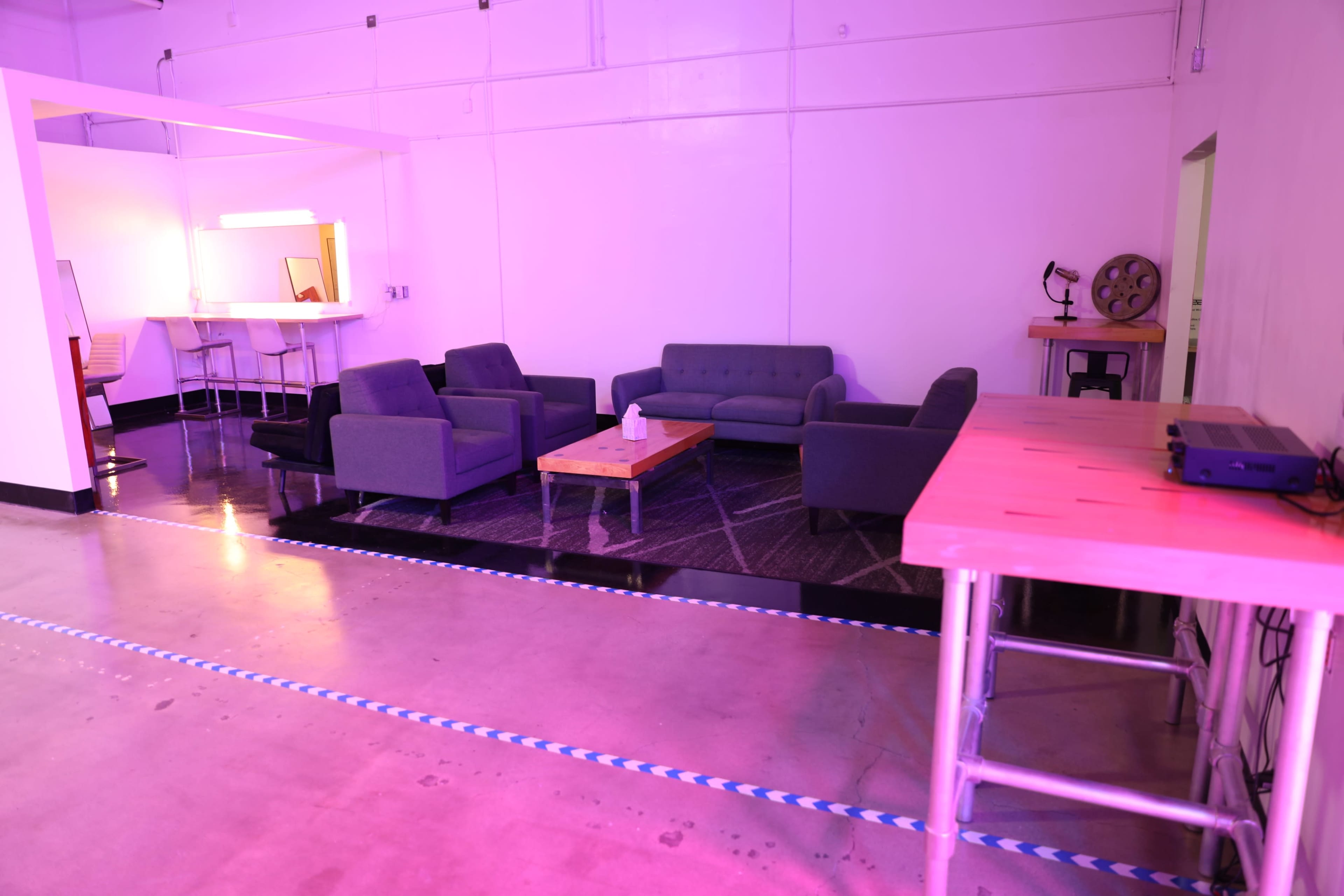 A spacious room with modern gray furniture, including sofas and a coffee table, illuminated with soft purple lighting.