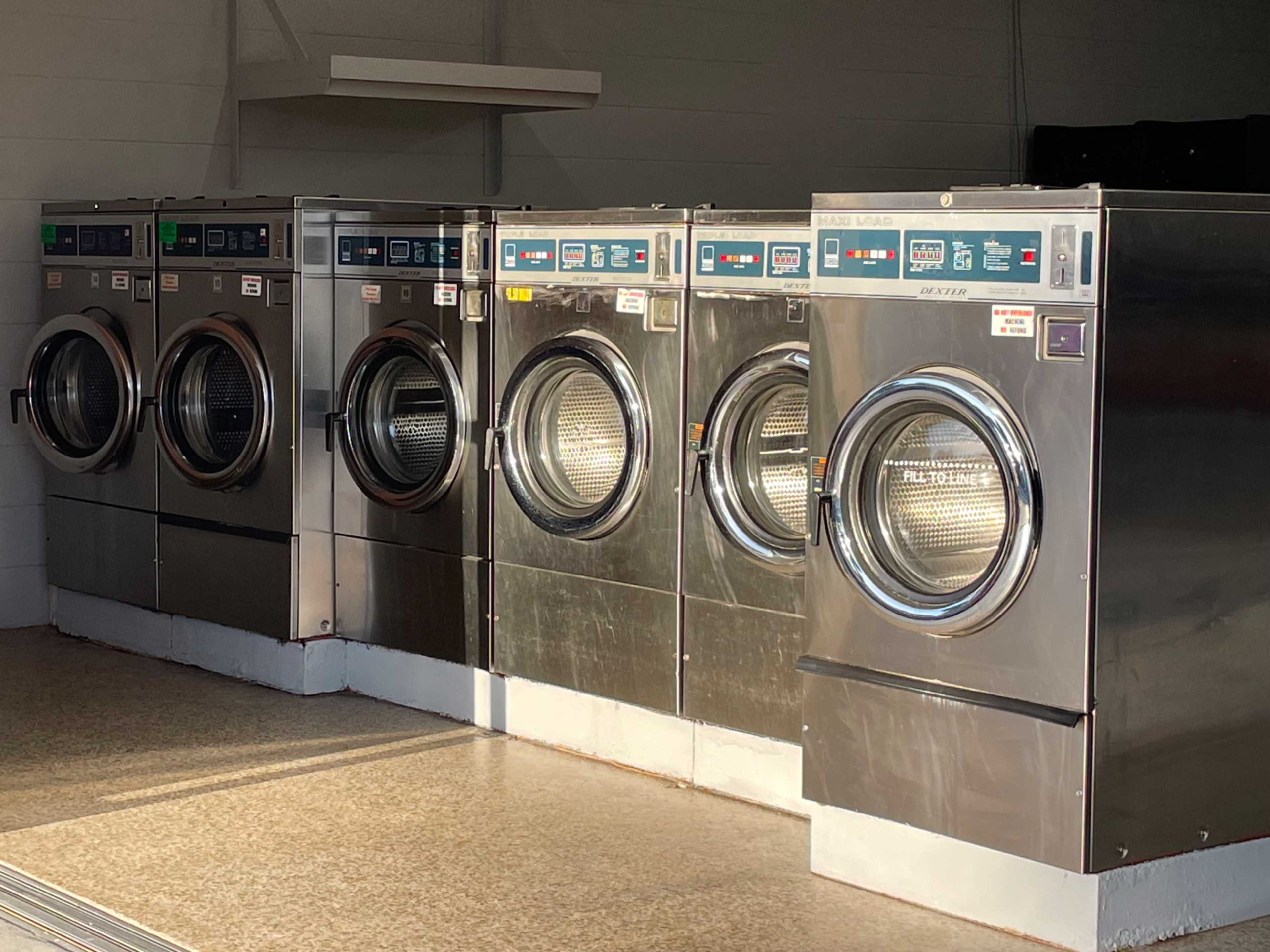 The image shows a row of five commercial washing machines lined up in a laundromat.