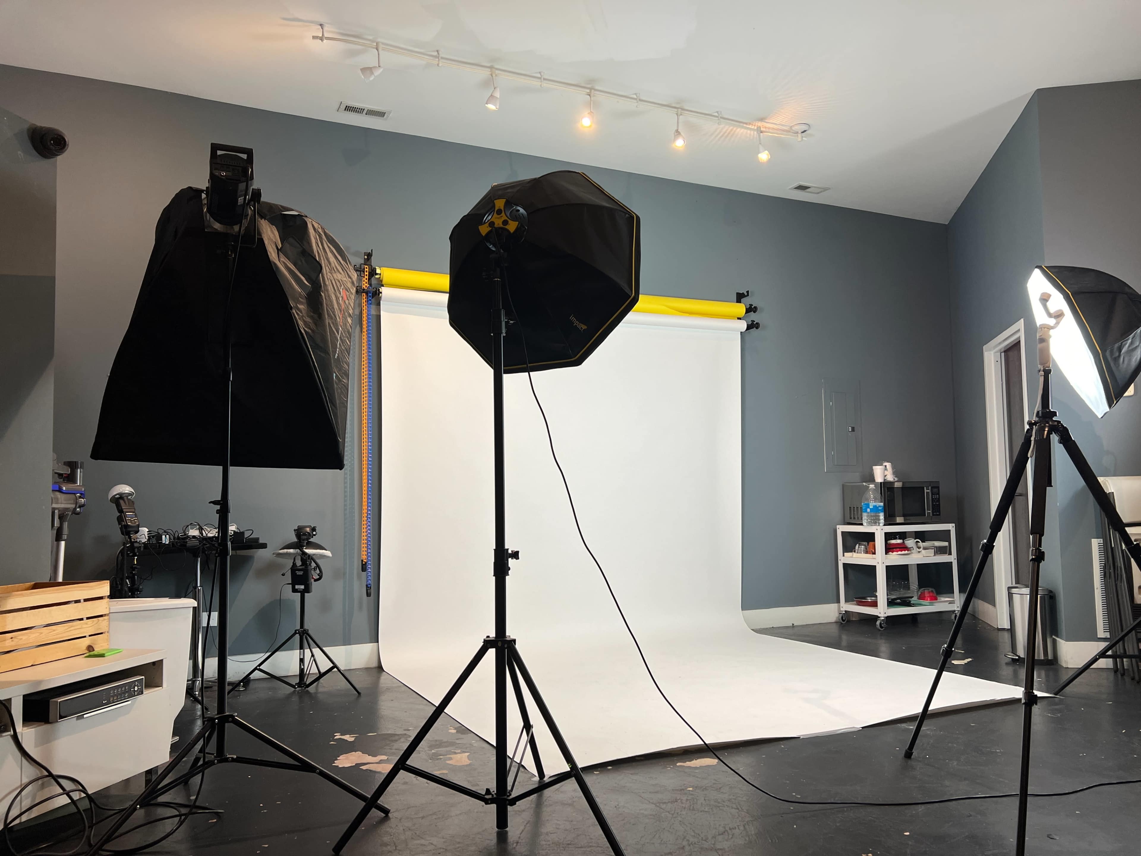 A photography studio is set up with softbox lighting on either side and a white backdrop in the center.