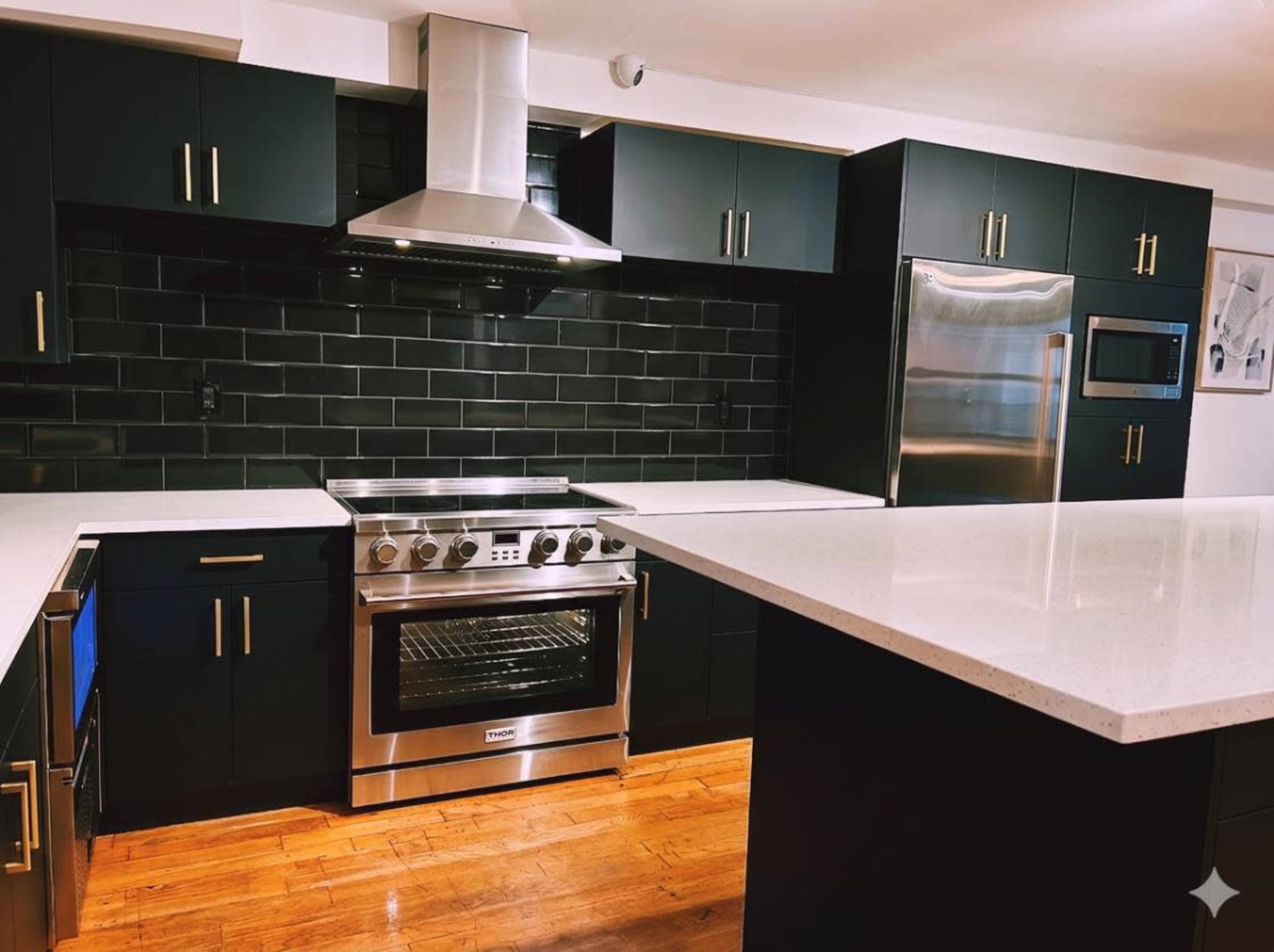 The image shows a modern kitchen featuring black cabinetry, a stainless steel oven, and a large island with a white countertop.