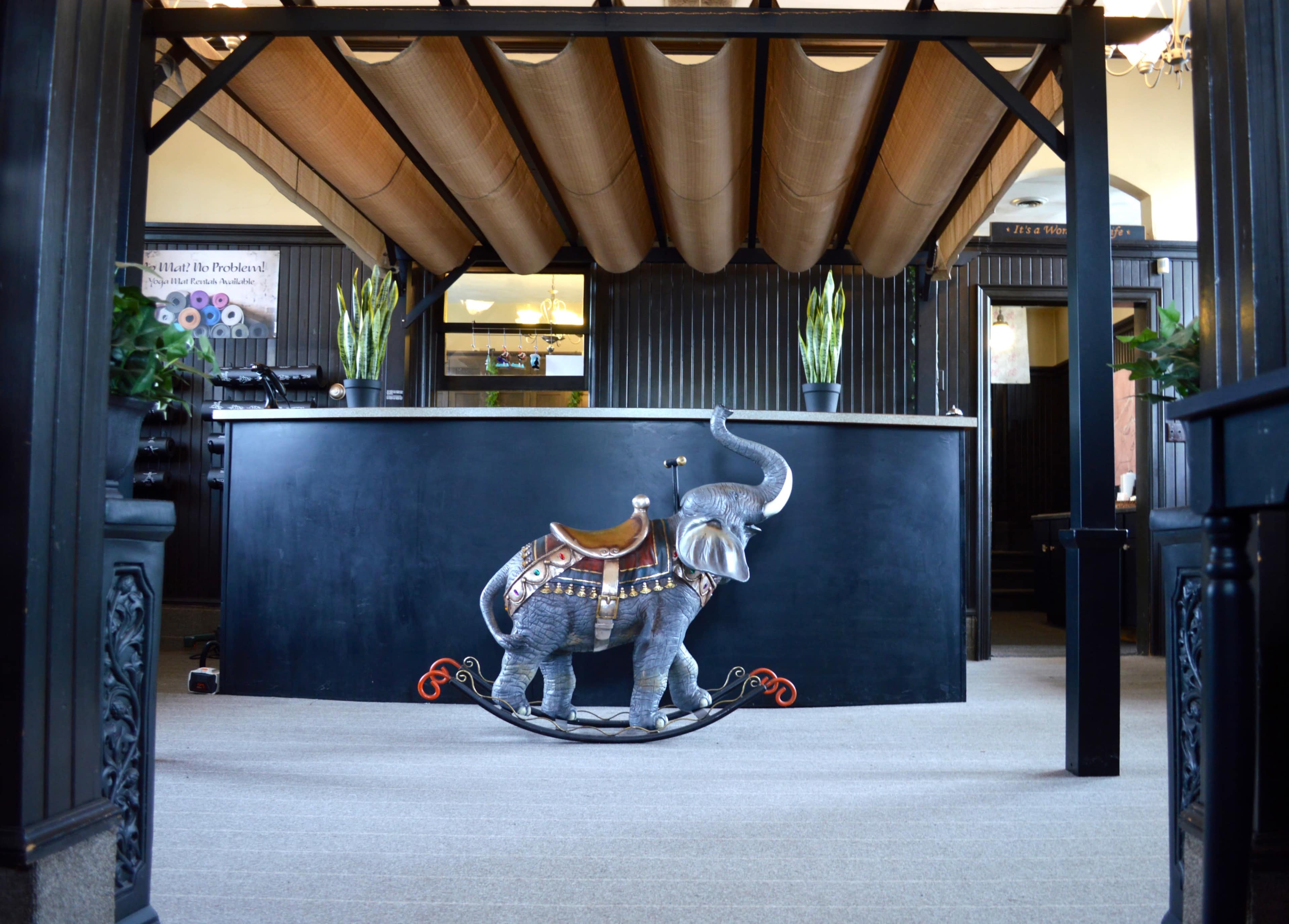 A reception area with a rocking elephant statue positioned in front of a black reception desk under a wooden ceiling.