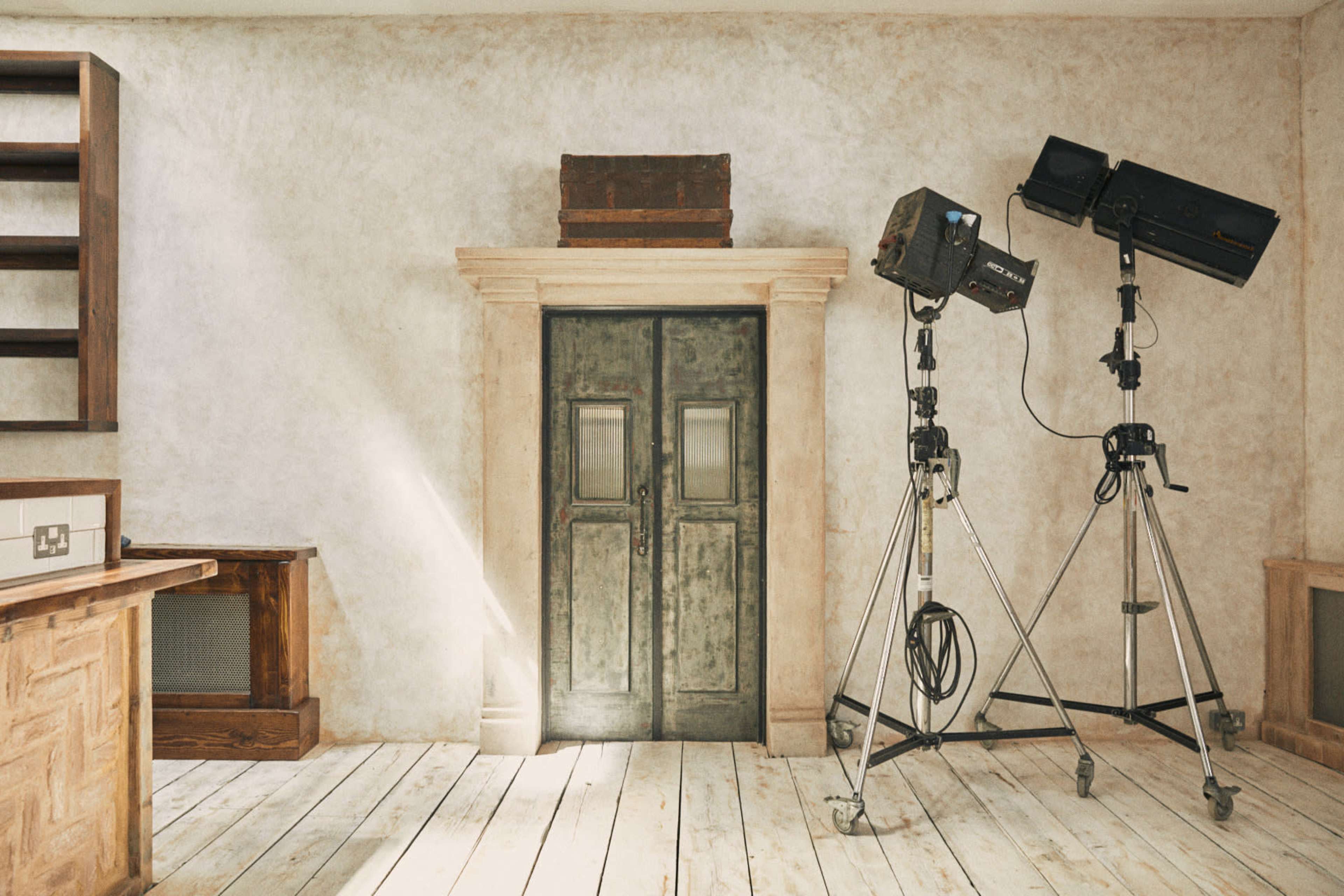 The scene shows a rustic room with wooden floors, a vintage double door, and two lighting stands set up beside the door.