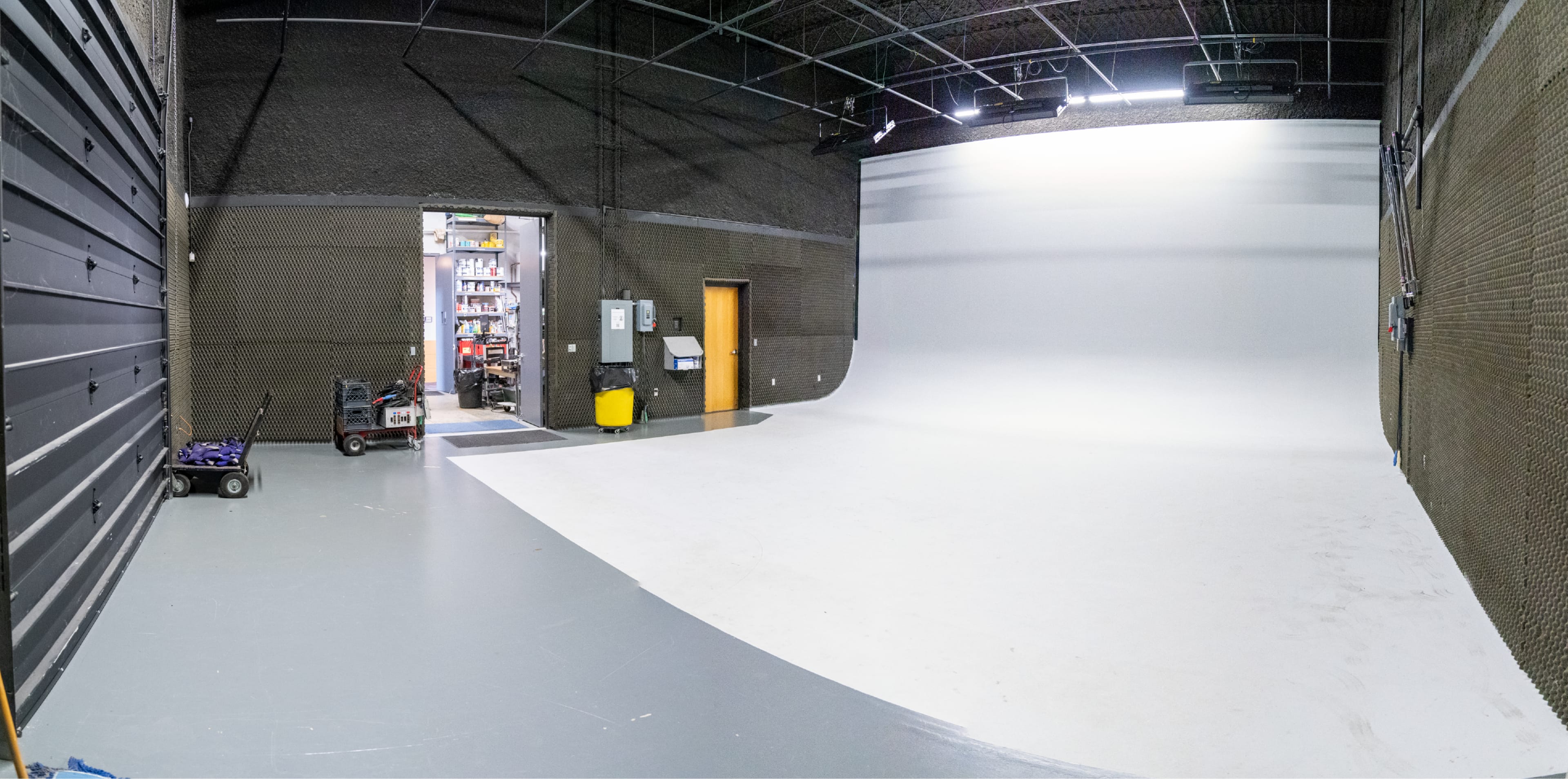 The image shows a large, empty studio space with a white backdrop and a doorway leading to a storage area.