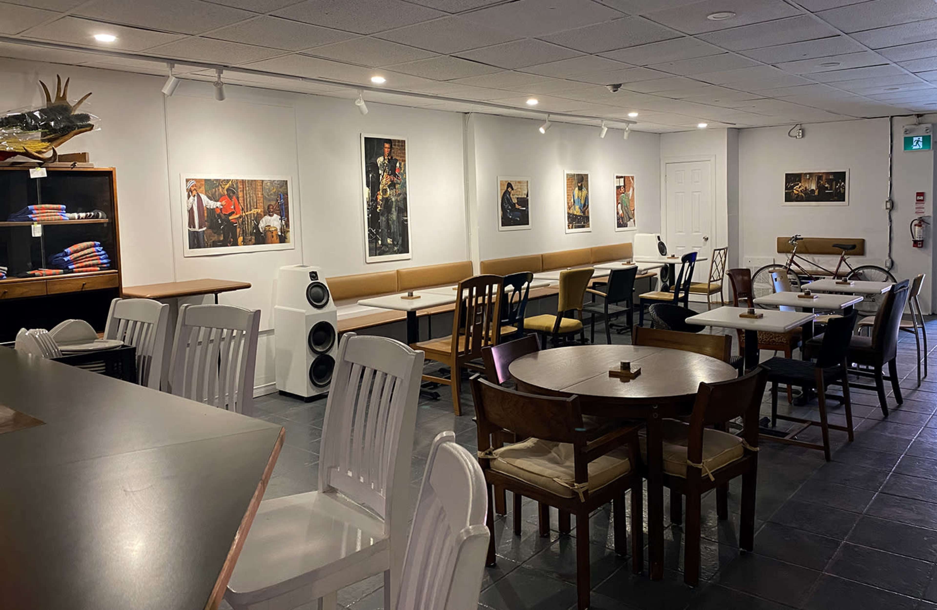 The image shows a spacious café interior with a mix of tables and chairs, featuring artwork on the walls and a counter in the foreground.