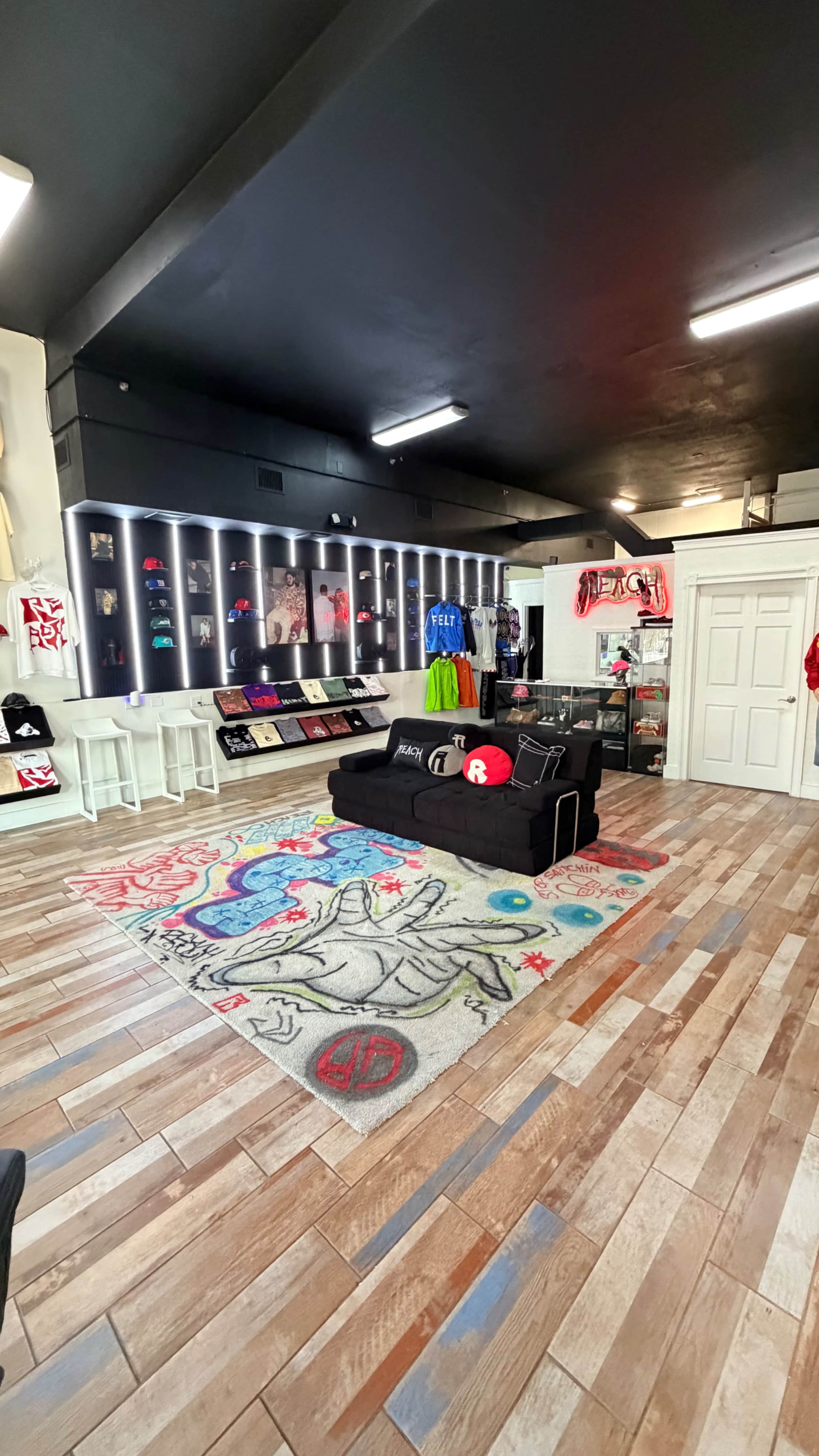 The image shows a modern retail space featuring a black couch, a decorative rug, and displays of clothing and accessories on the walls.