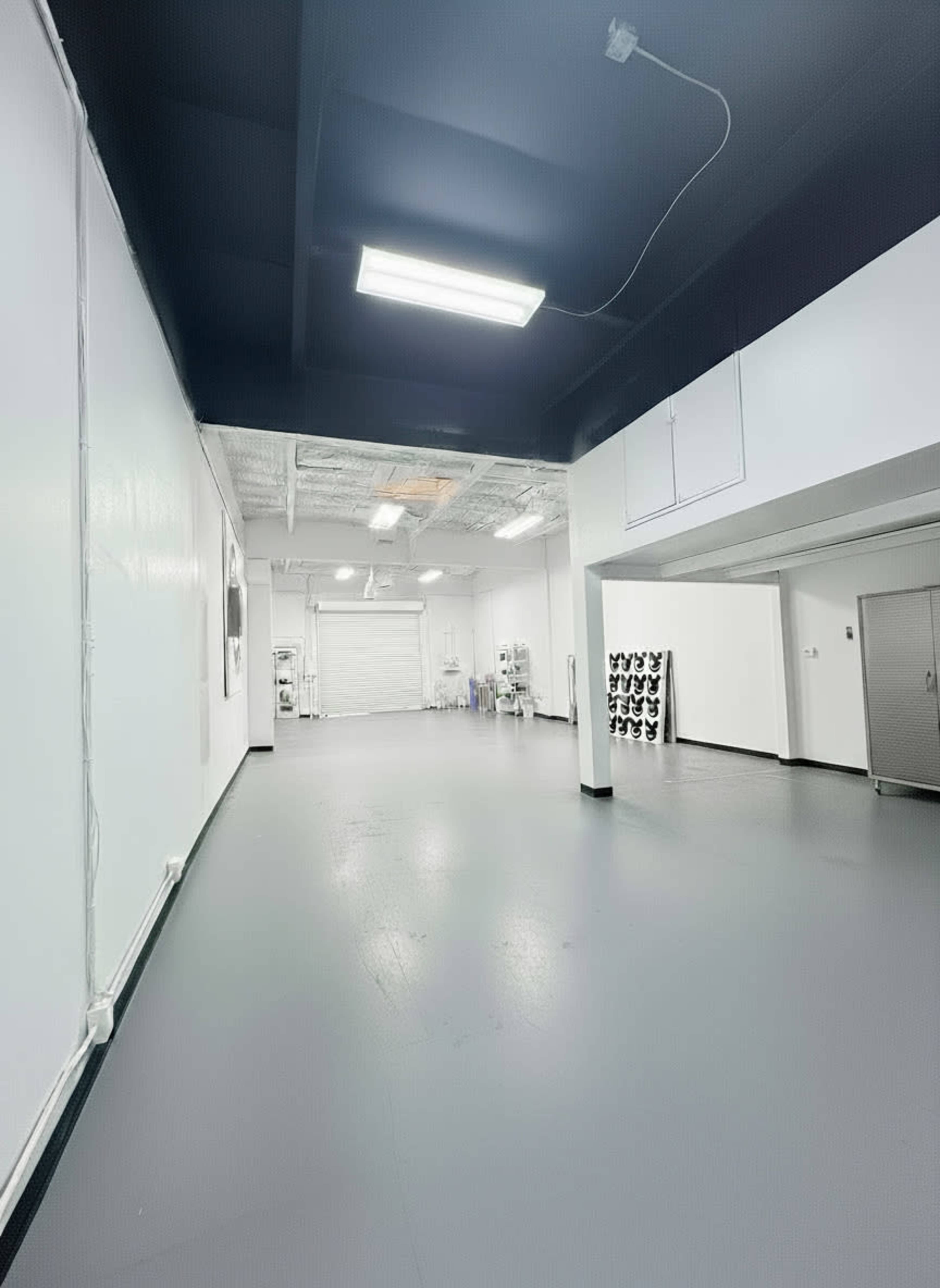 The image shows a spacious, well-lit interior of a modern warehouse or studio featuring gray flooring and white walls.