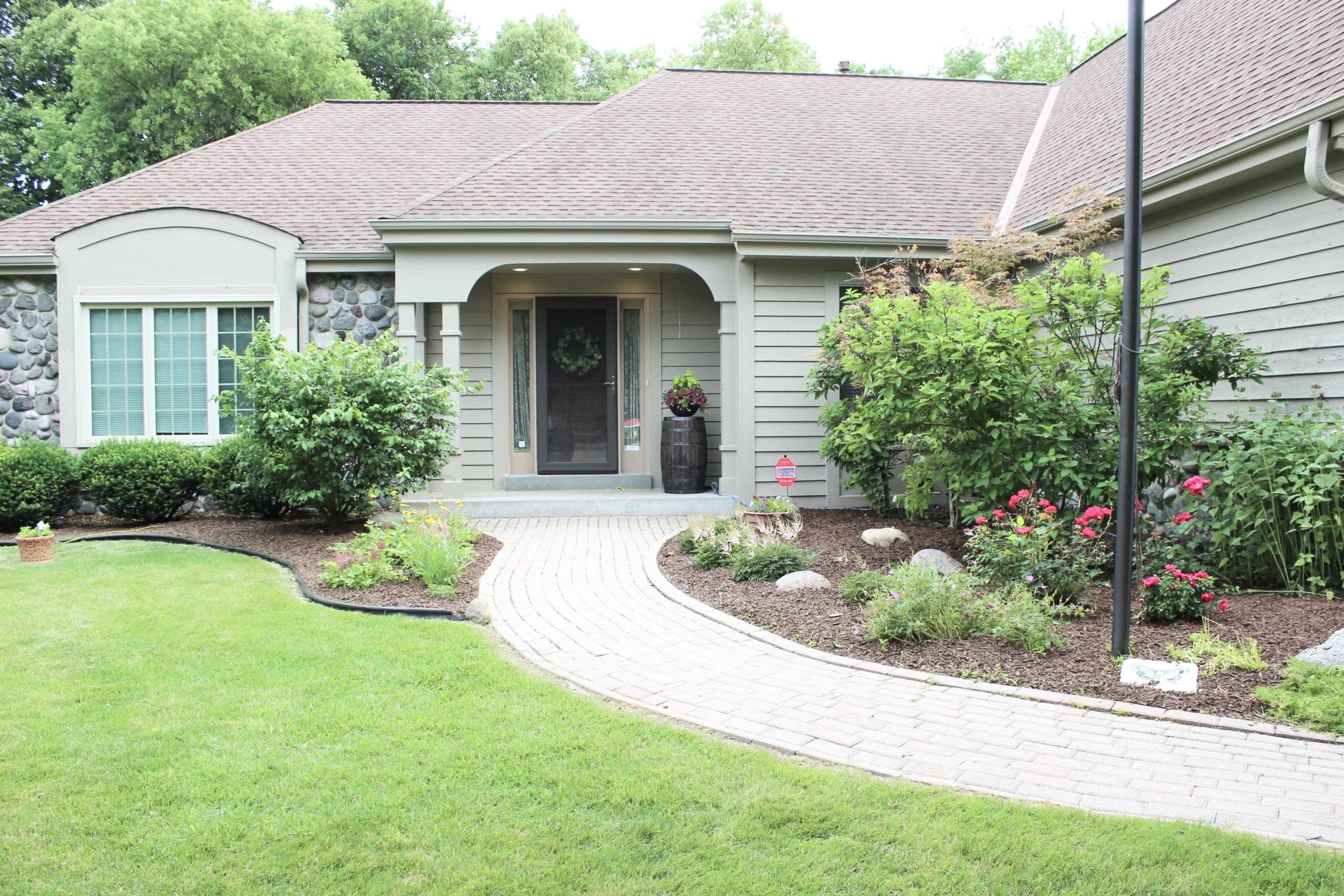 The image shows a landscaped front yard with a curved stone pathway leading to the entrance of a house.