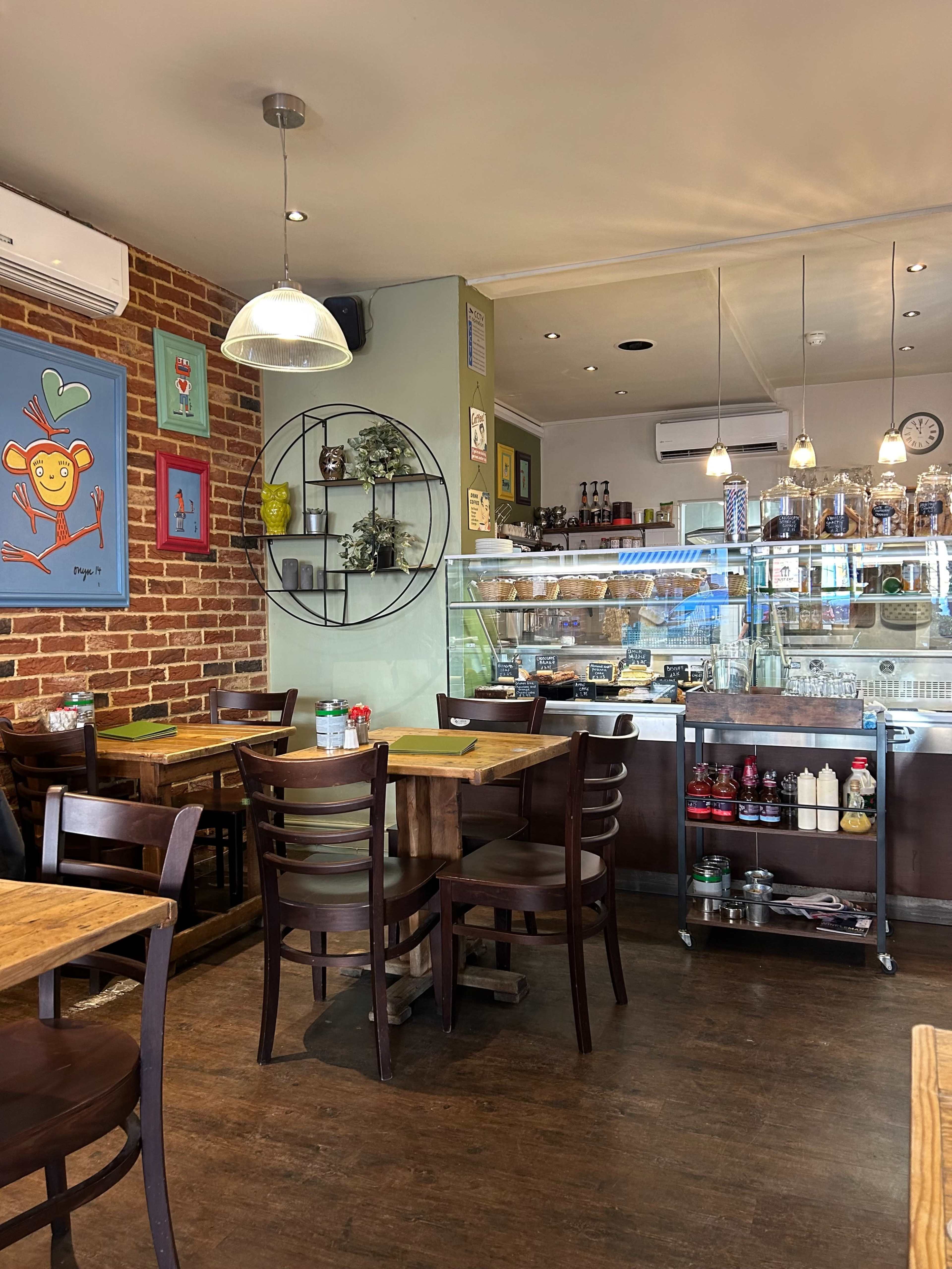 A cozy café interior featuring wooden tables and chairs, exposed brick walls, and a counter displaying various food items and beverages.